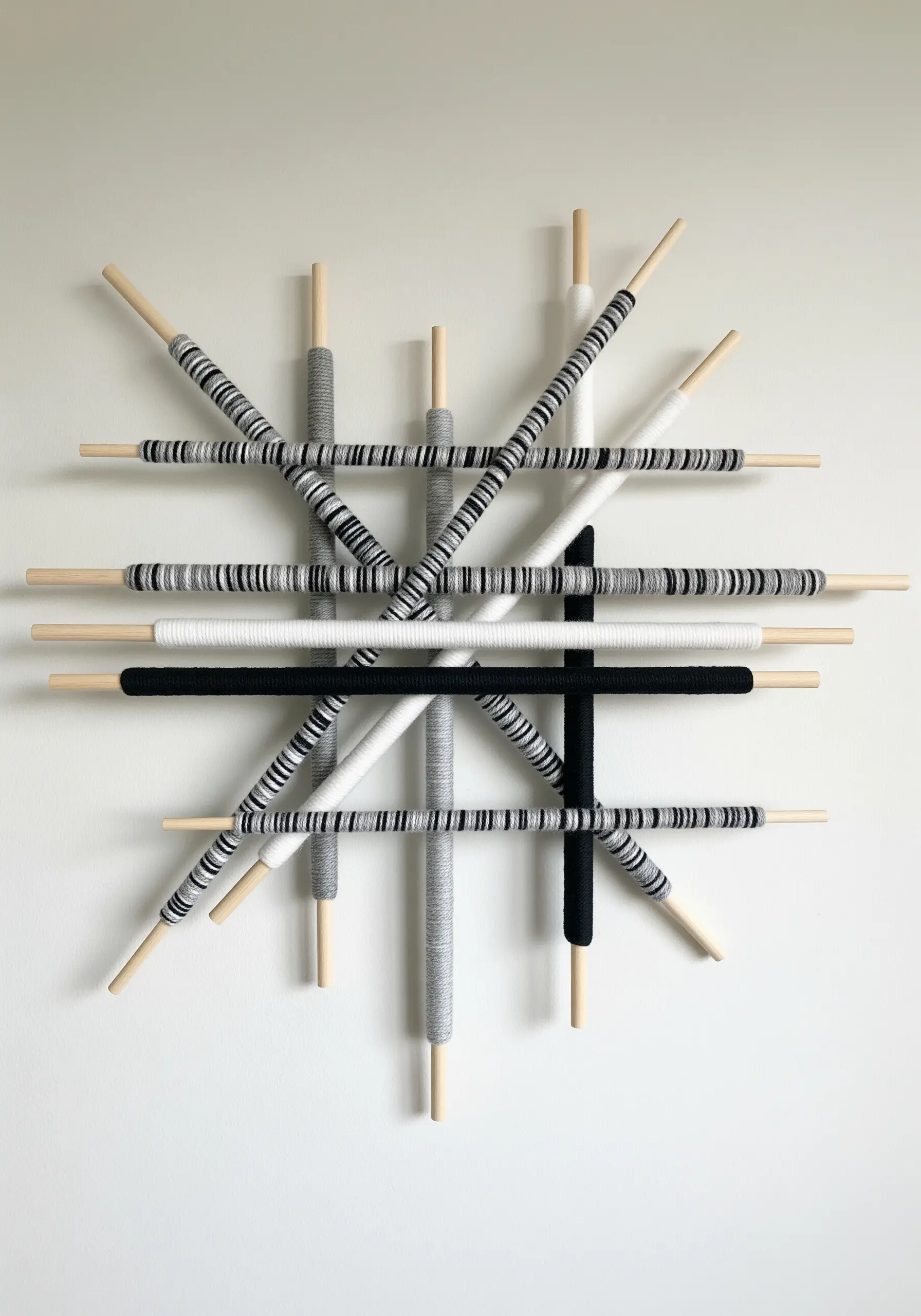 Interlocking wooden dowels wrapped in black, white, and grey yarn form a geometric wall sculpture.