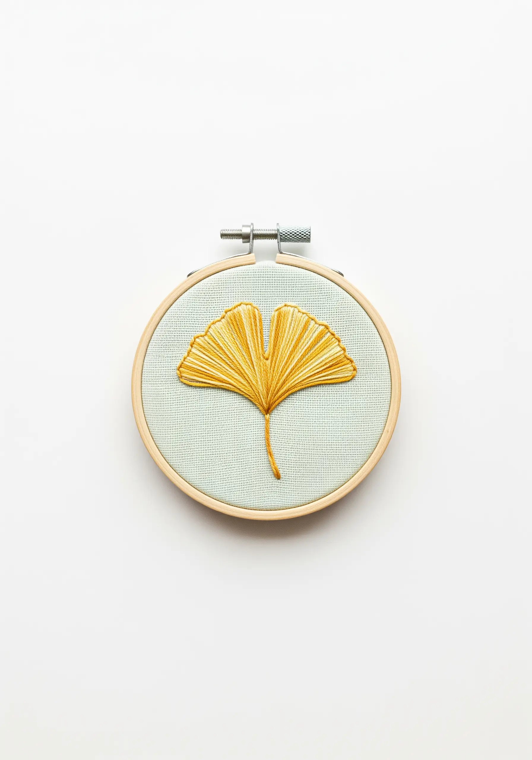 Golden yellow embroidered ginkgo leaf on light green fabric in a small hoop.