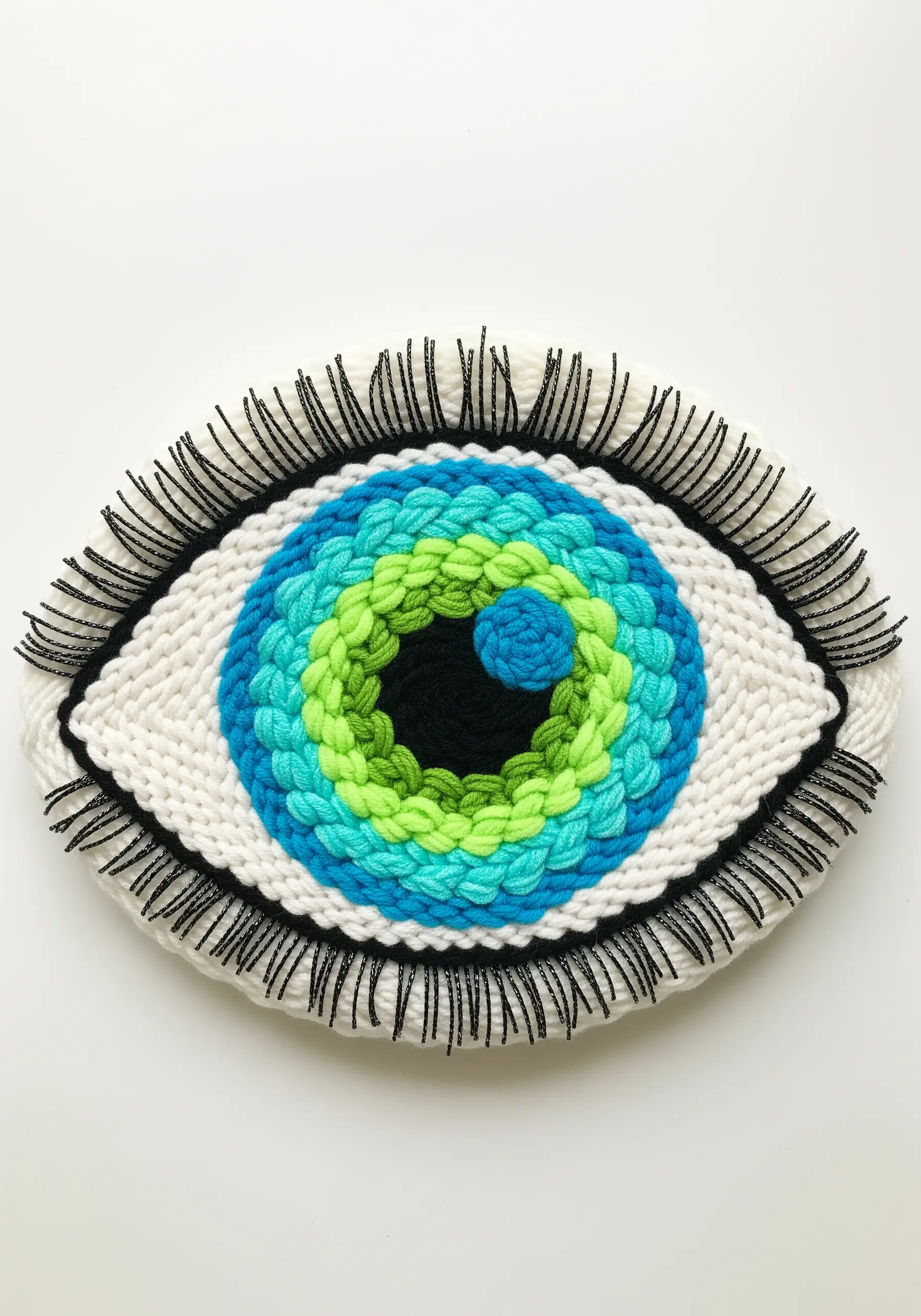 A woven eye in blue and green hues with dramatic black thread eyelashes.