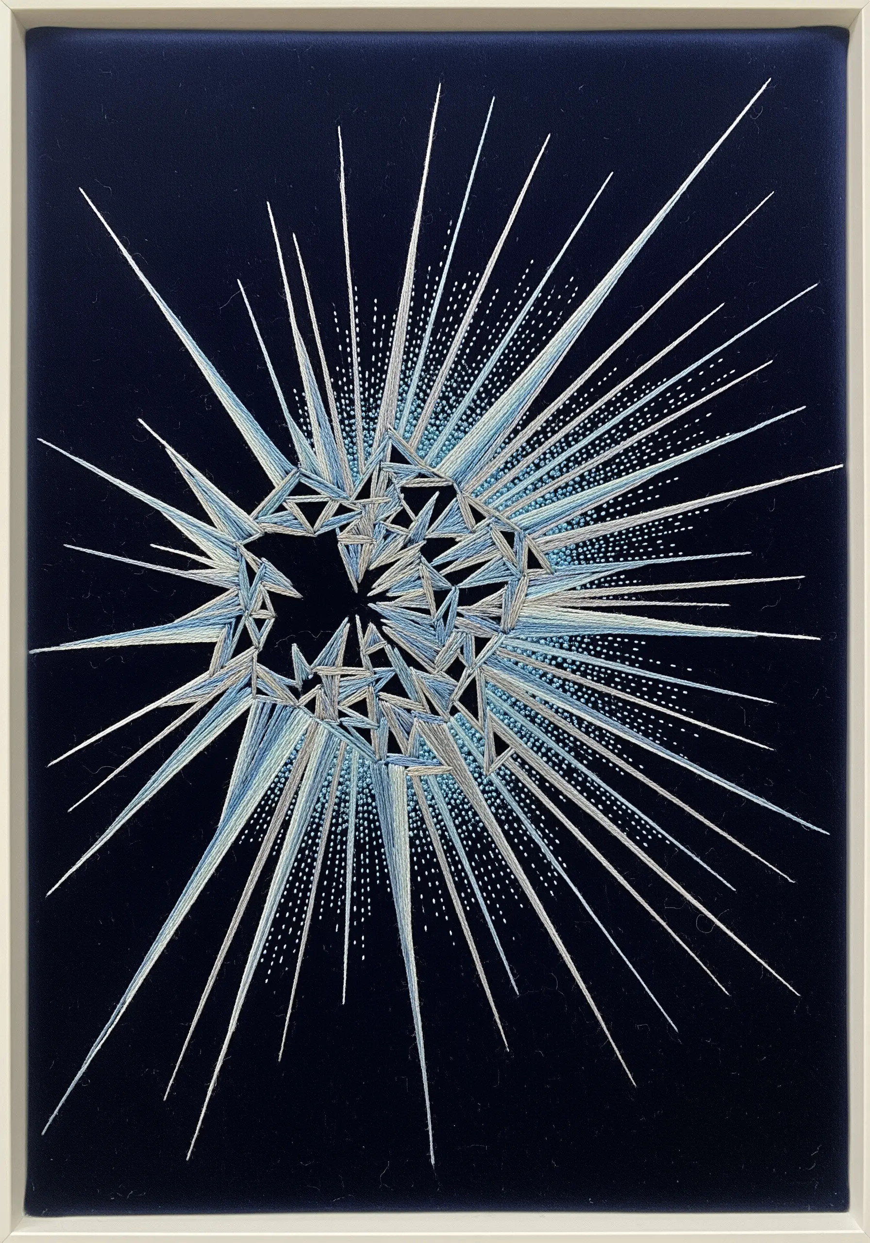 Abstract starburst embroidery with geometric shards in silver and blue on navy fabric.
