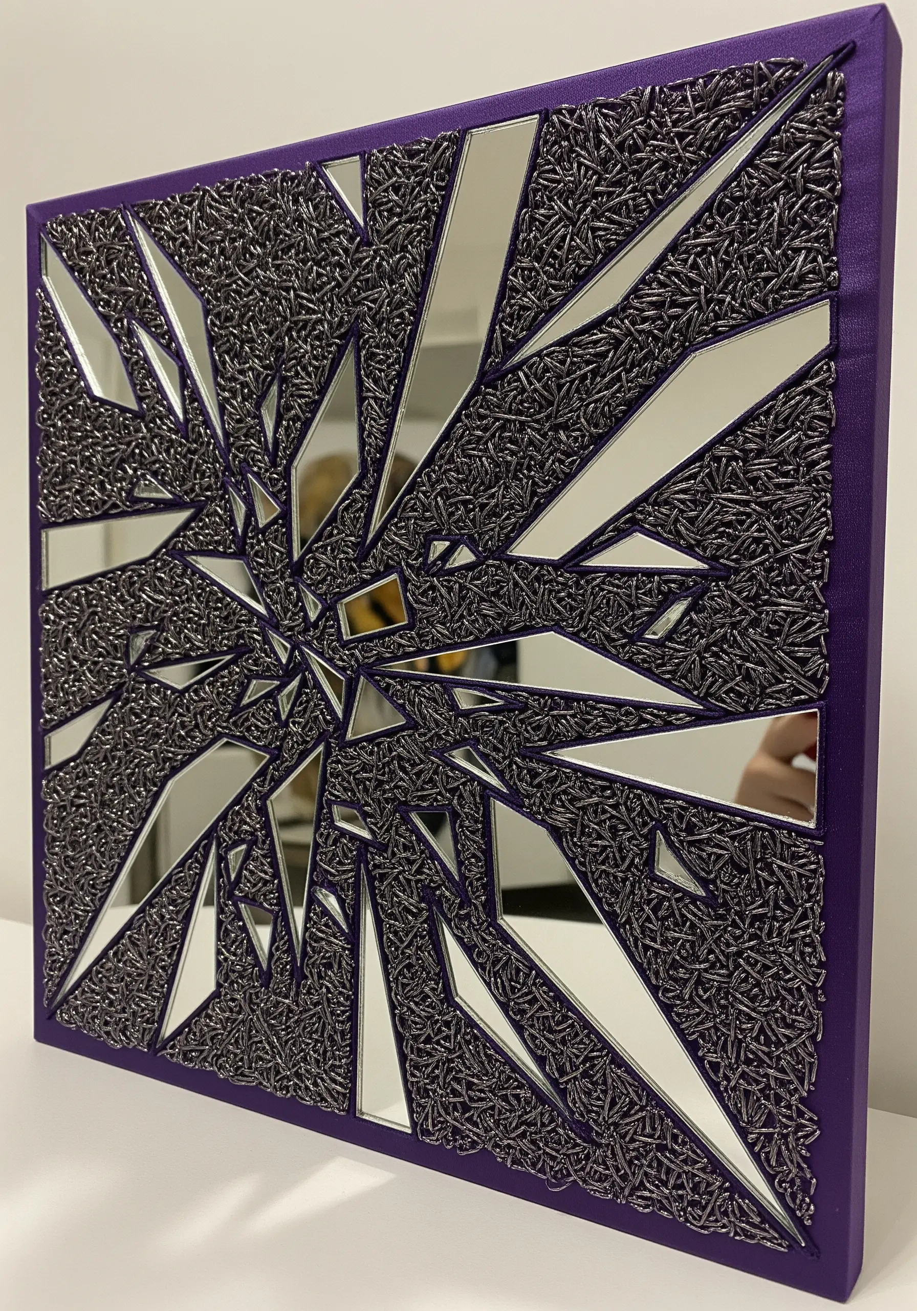 A mixed-media piece with mirror shards and dense silver metallic embroidery.