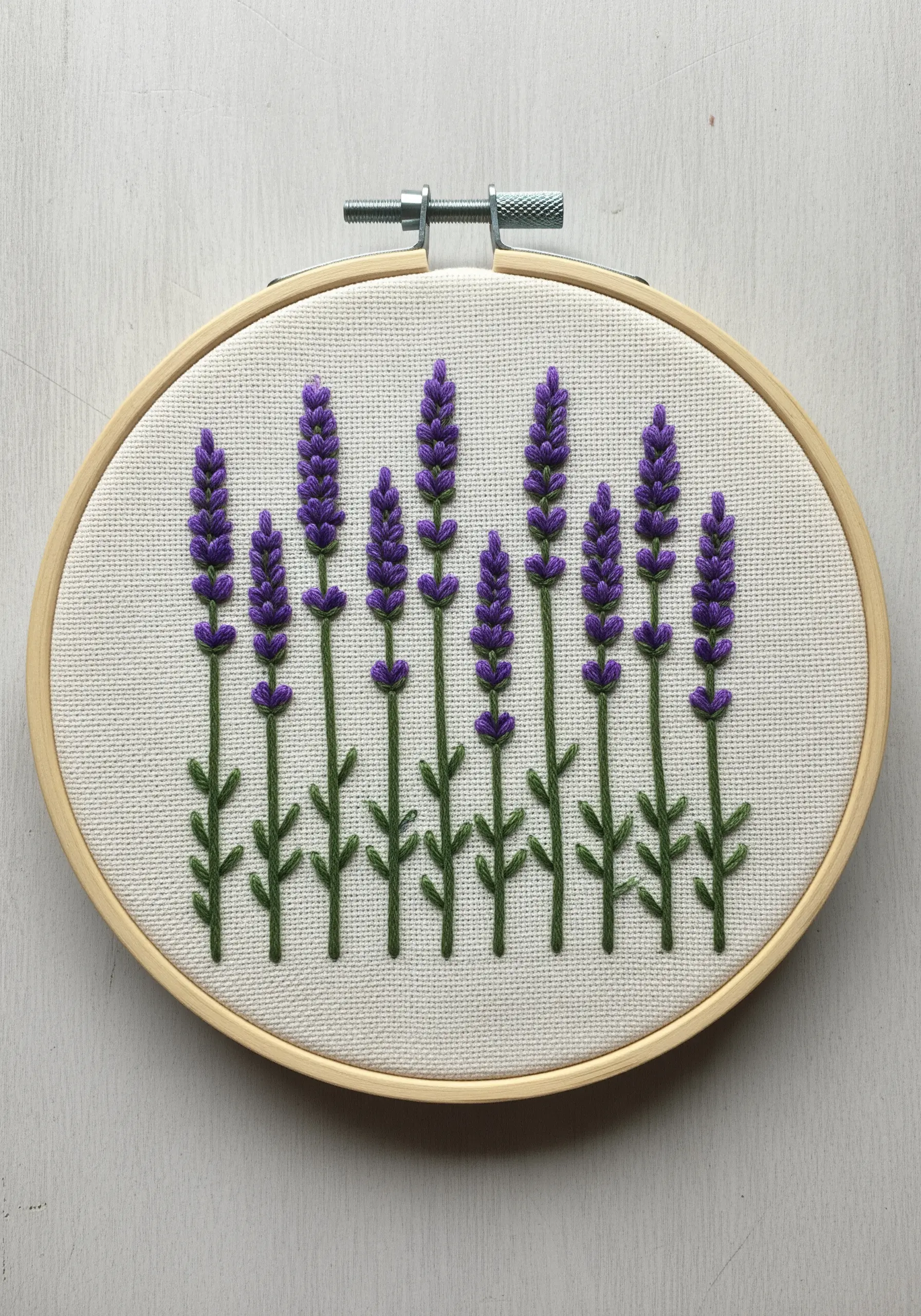 Embroidered lavender sprigs in an oval hoop using French knots and straight stitches.