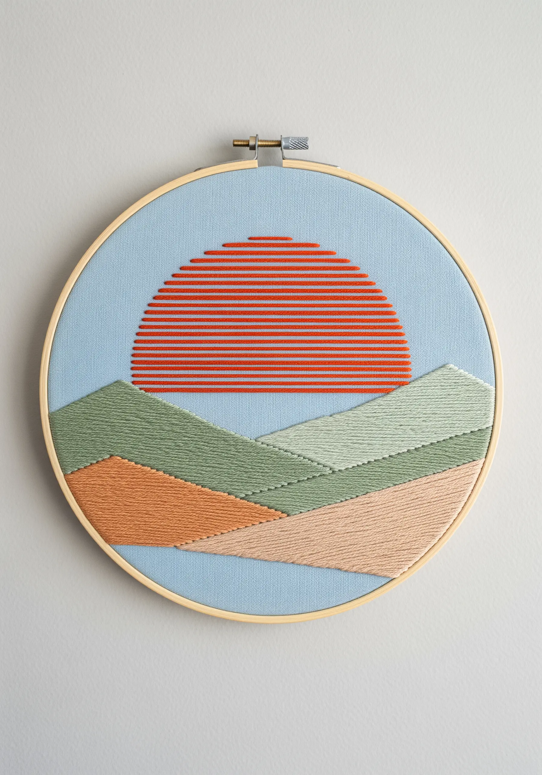 A minimalist landscape with a red setting sun and hills in green and peach satin stitch.