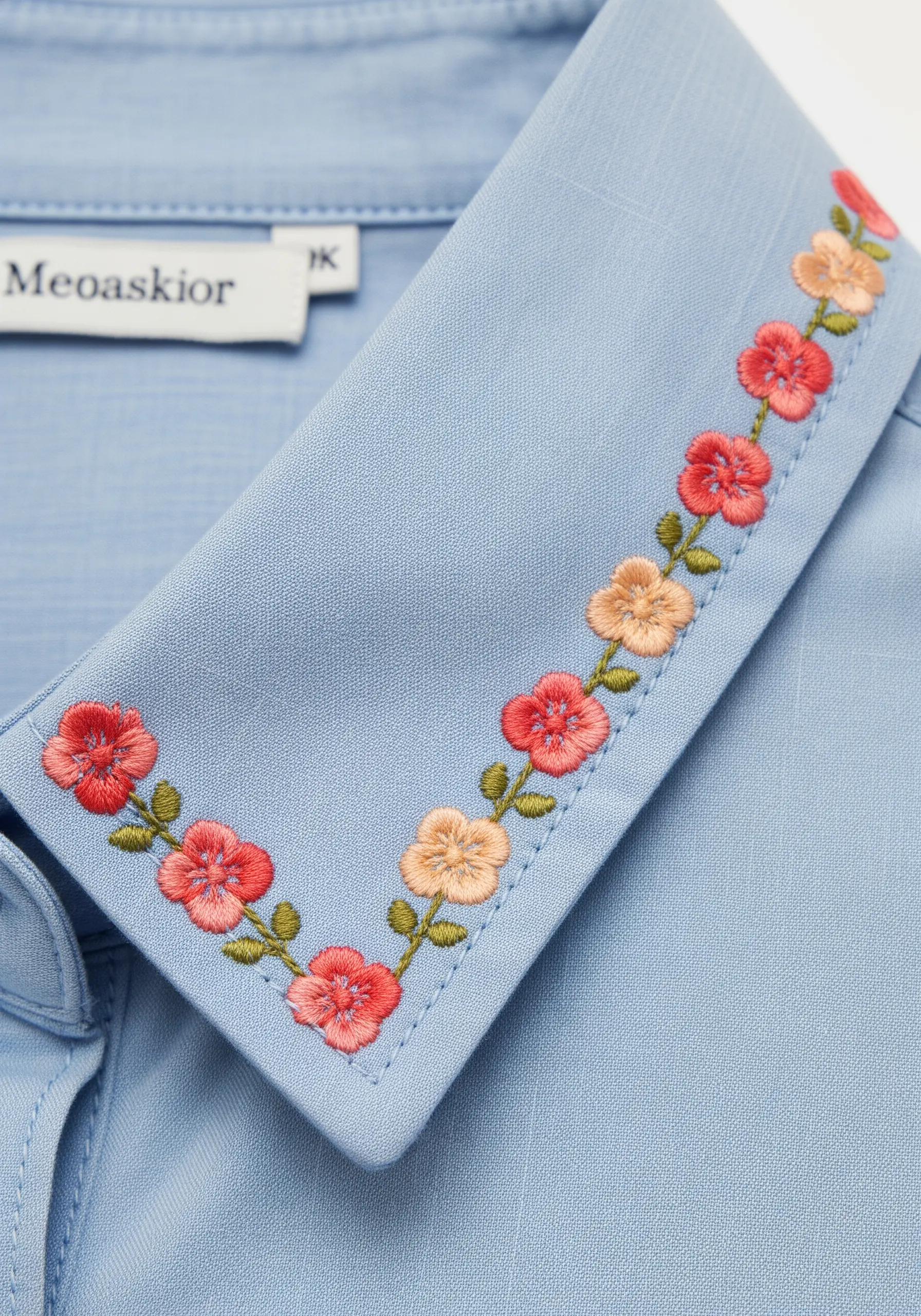 A light blue shirt collar with a delicate border of tiny embroidered flowers in a coral-to-peach gradient.