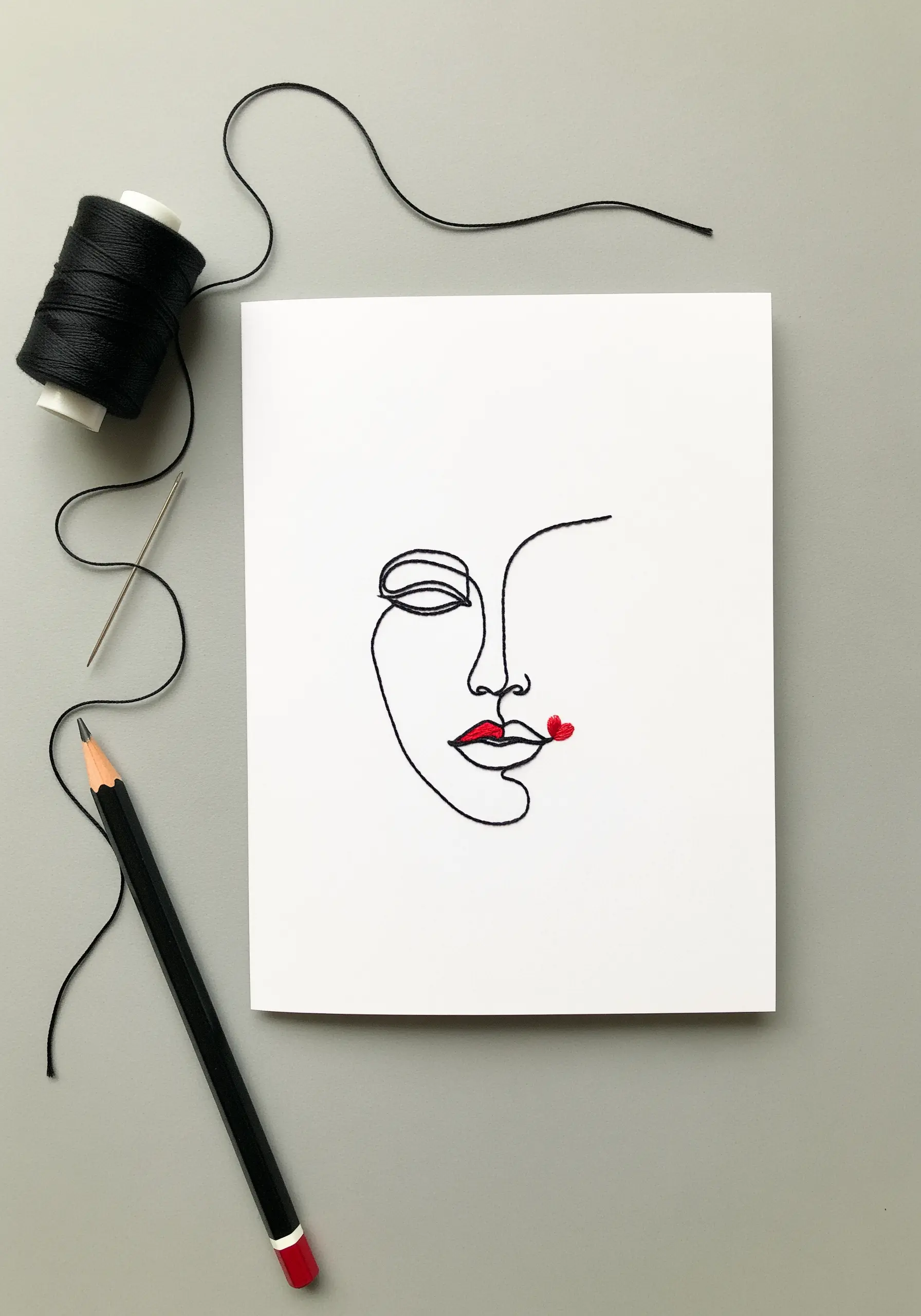 A minimalist single-line embroidery of a face with small red heart-shaped lips.