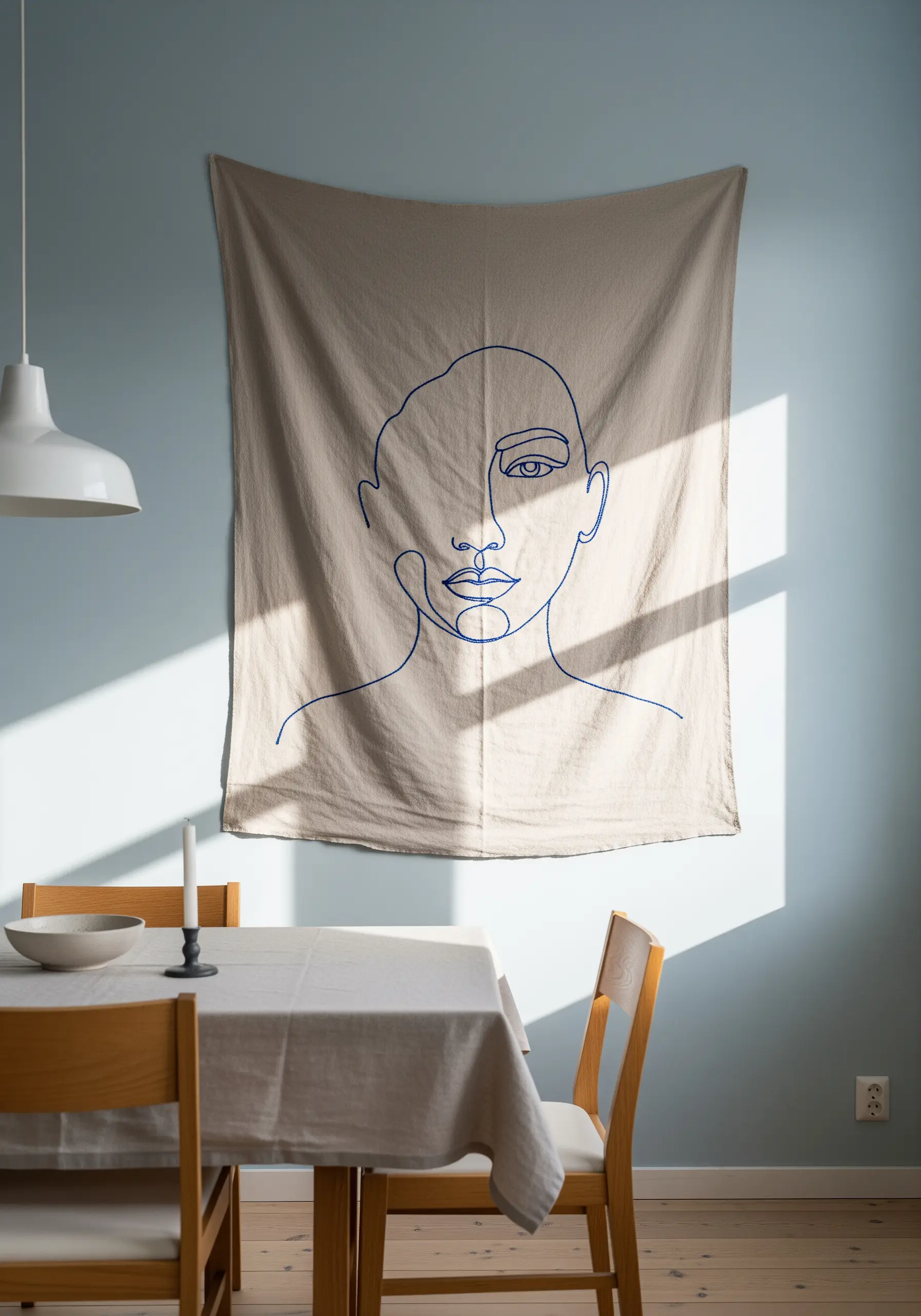 A large-scale, single-line embroidered face portrait on a neutral linen wall hanging.