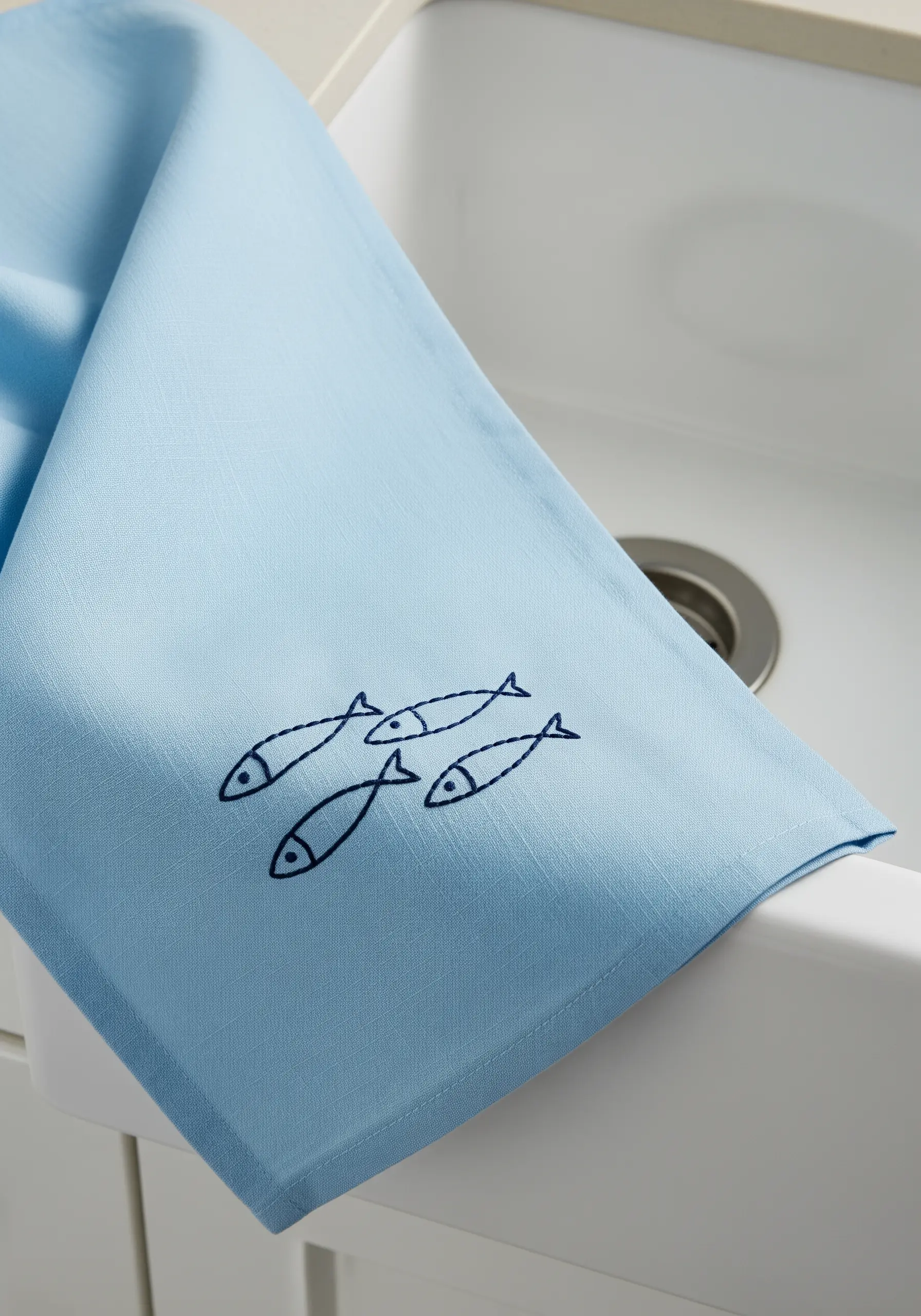 Four simple fish outlines embroidered in navy blue on a light blue kitchen towel.