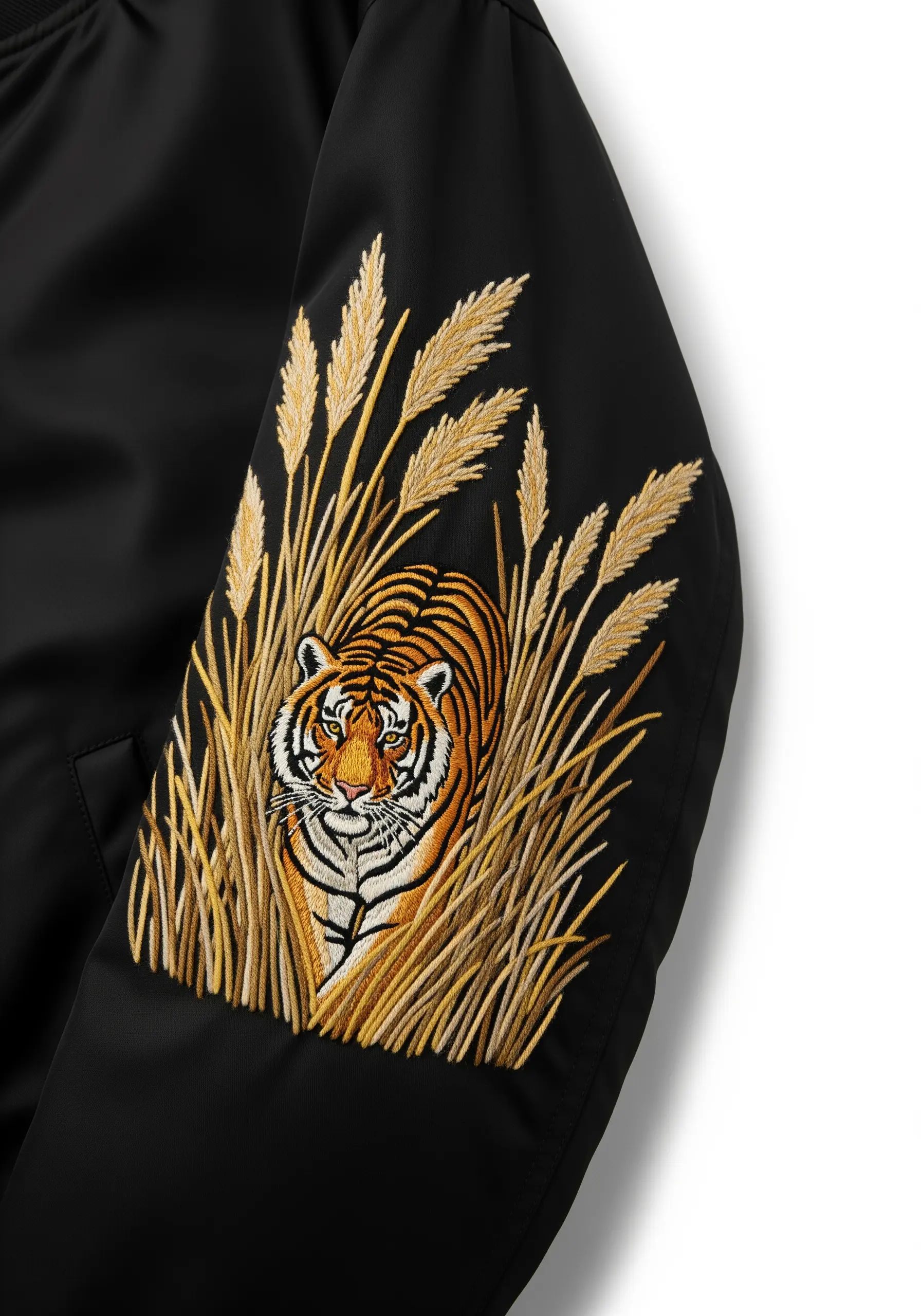 Tiger embroidered on the sleeve of a black jacket, peeking through tall golden grass.
