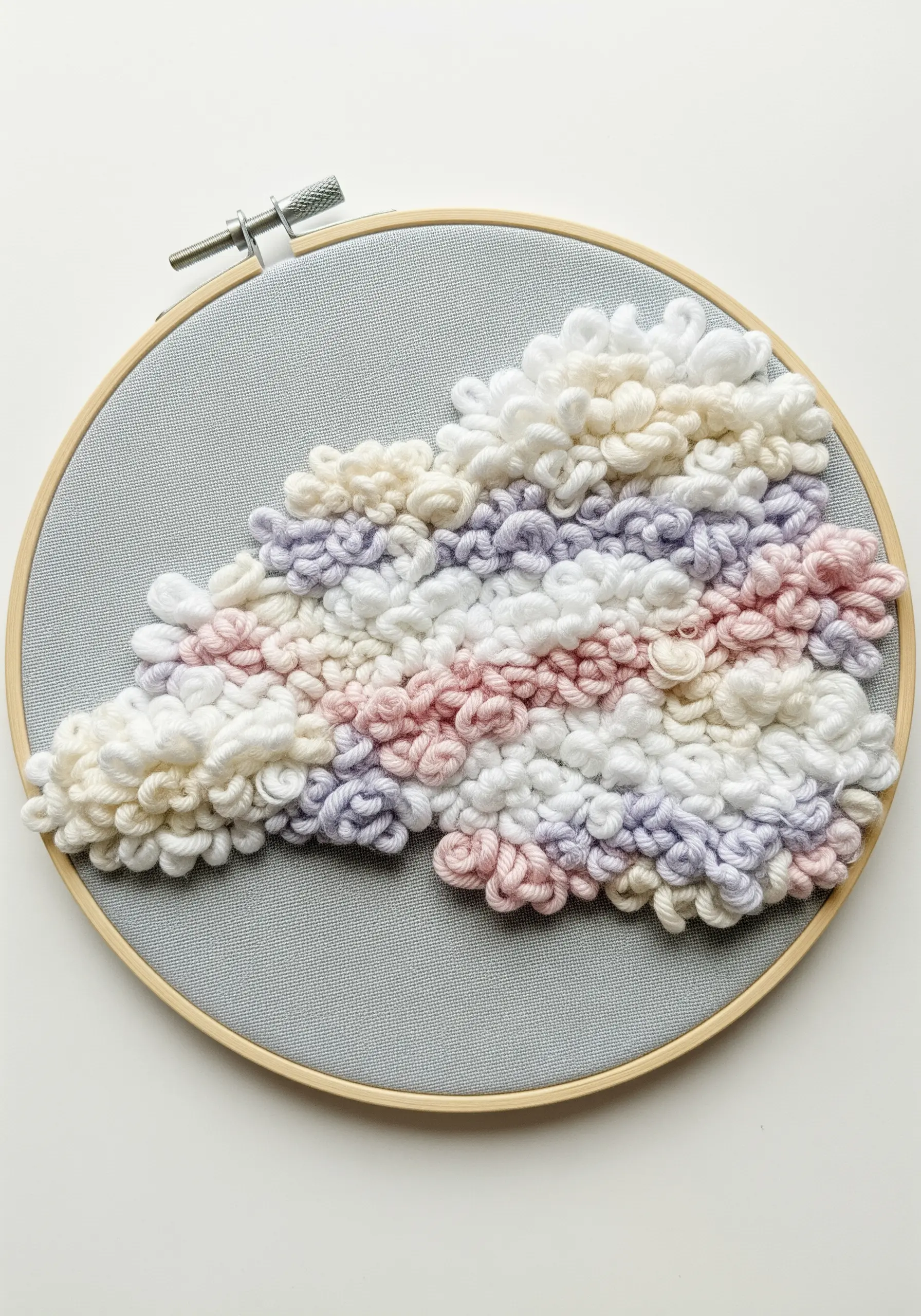 A thick, plush cloud shape made with punch needle technique in pastel yarns on gray fabric.