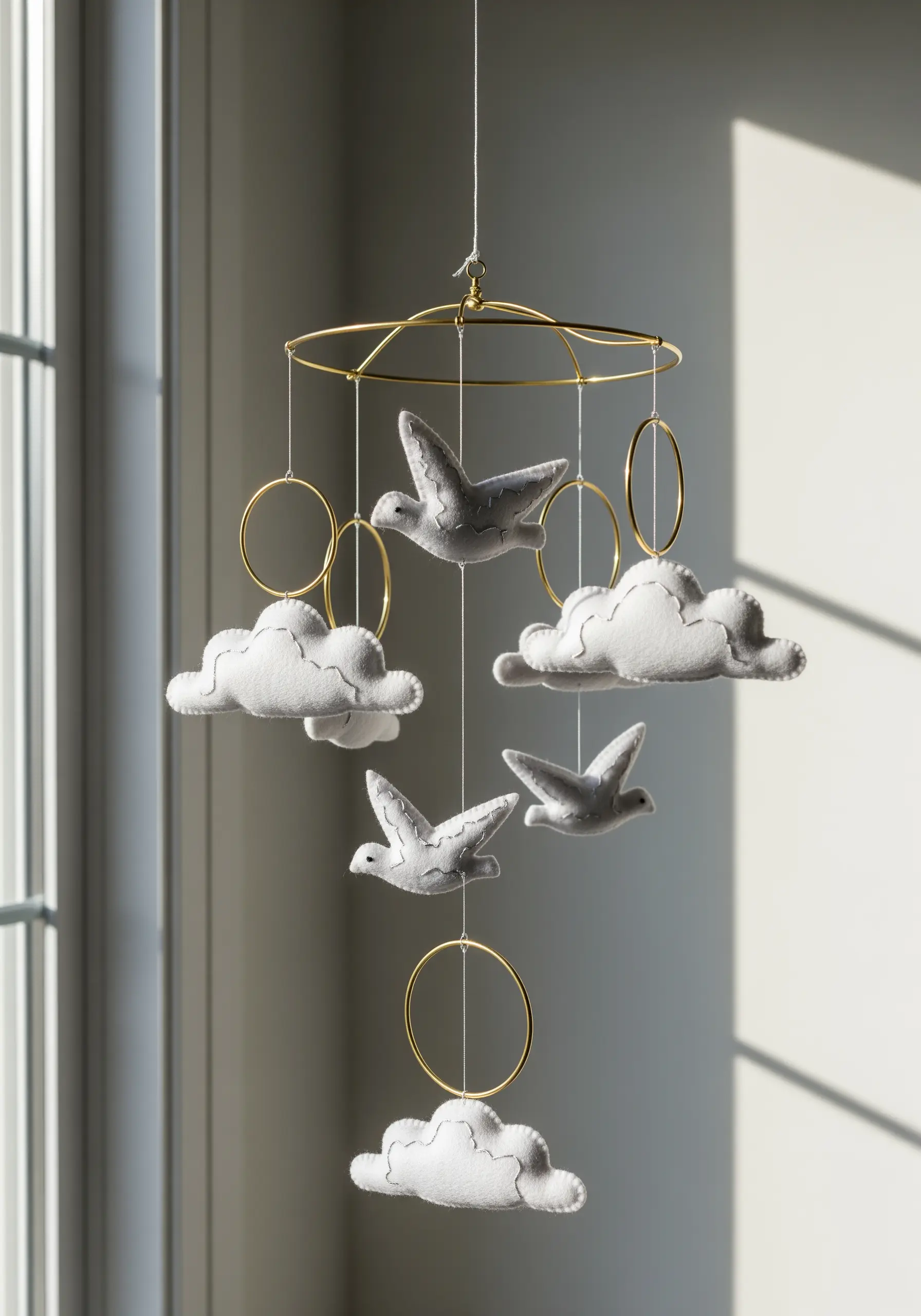 Nursery mobile with hand-stitched felt birds and clouds hanging from a gold frame.