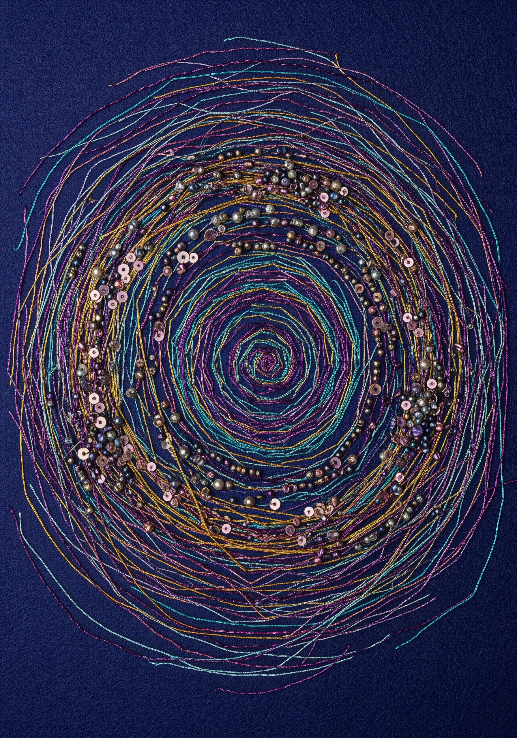 A spiral of couched multicolored metallic threads embellished with beads and sequins on navy fabric