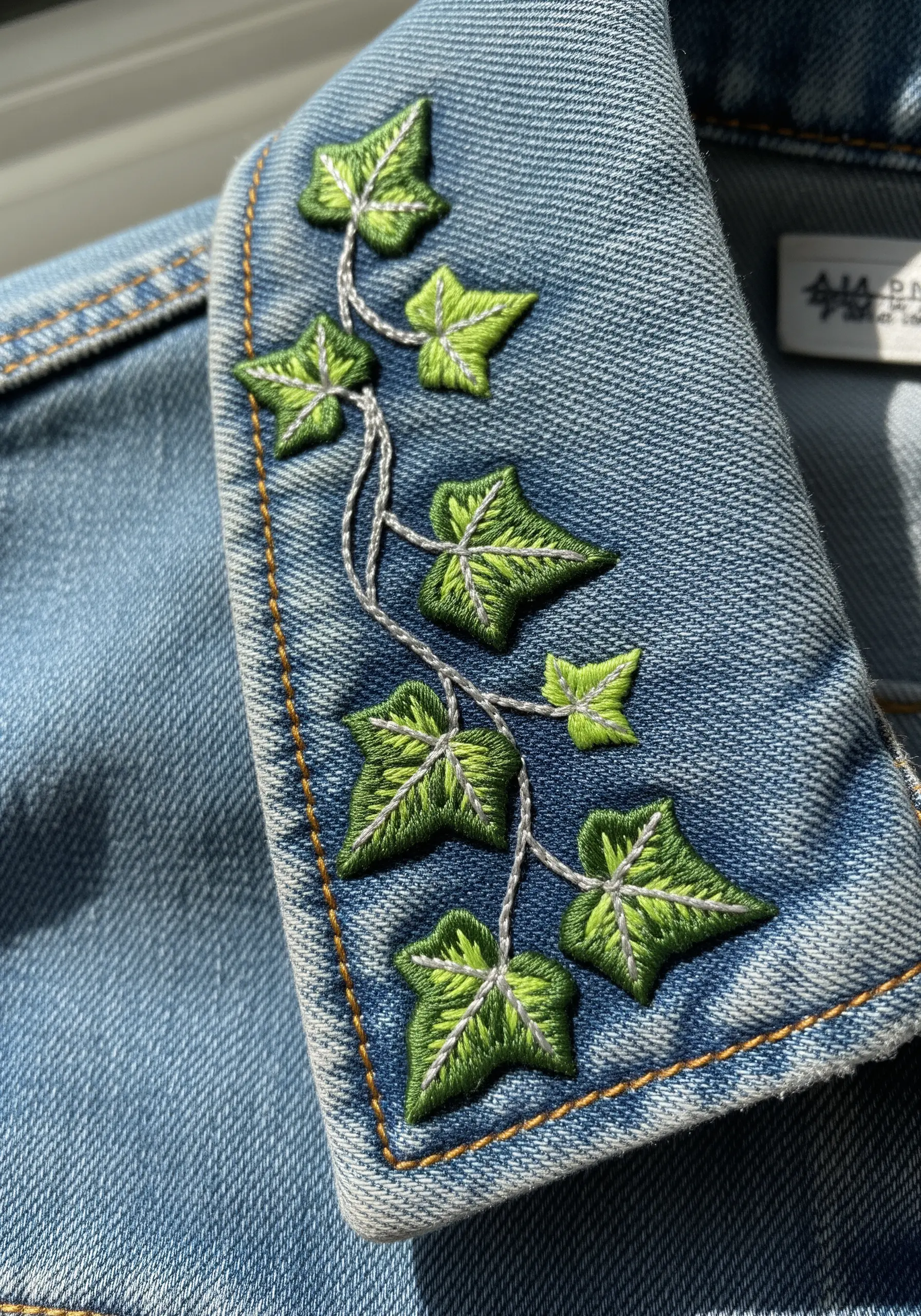 Small ivy leaves with two-tone green satin stitch on a denim jacket collar.