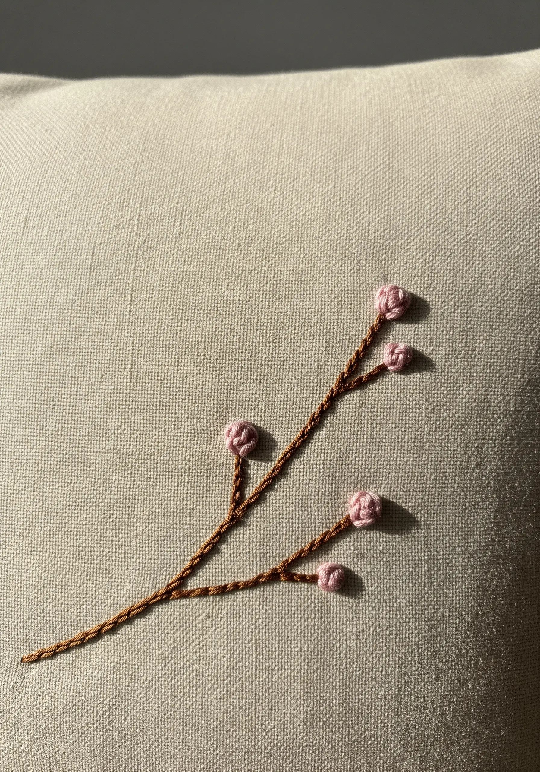 An embroidered branch with small, textured pink flower buds made from bullion knots.