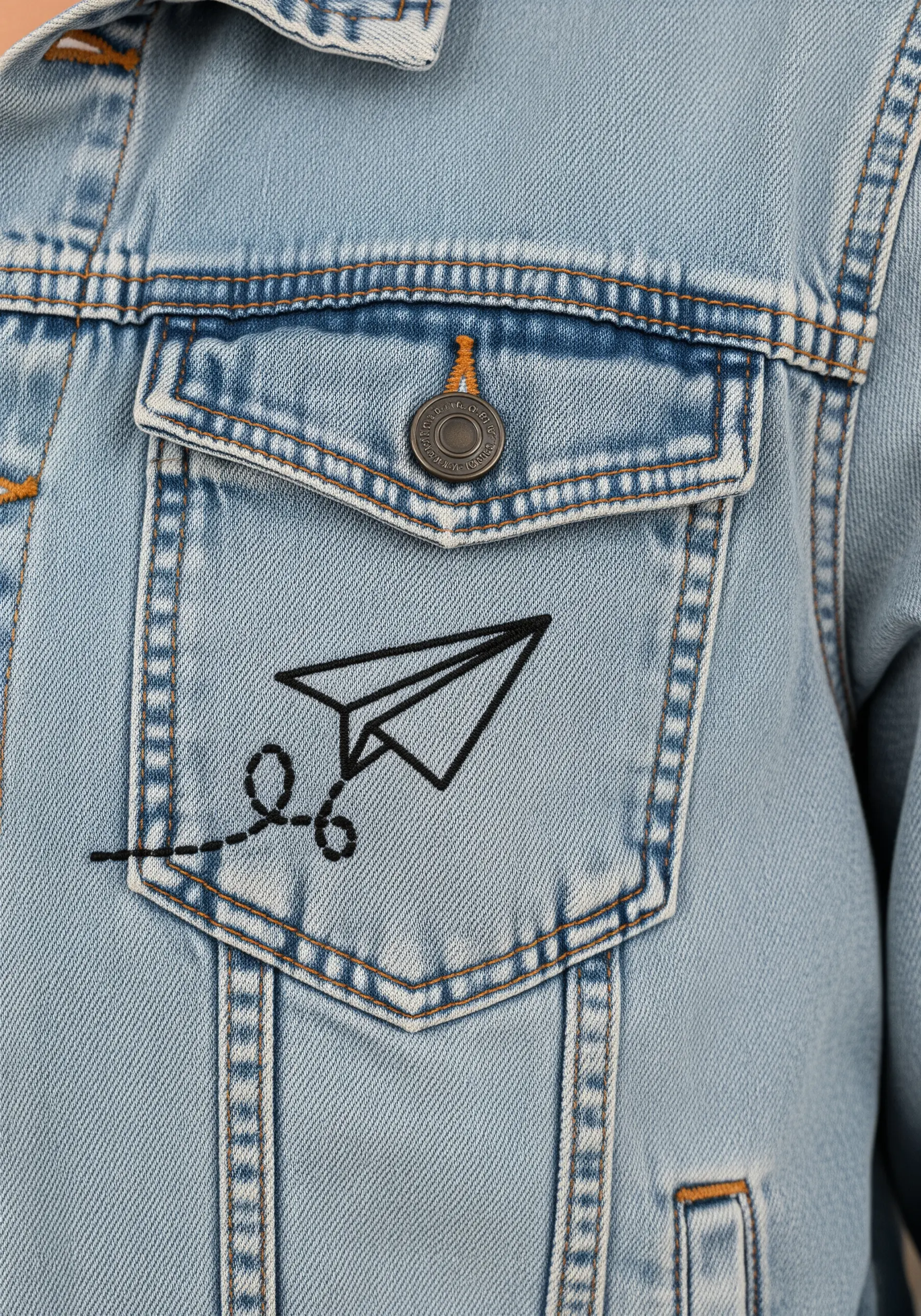 A minimalist black outline of a paper airplane stitched onto the pocket of a denim jacket.