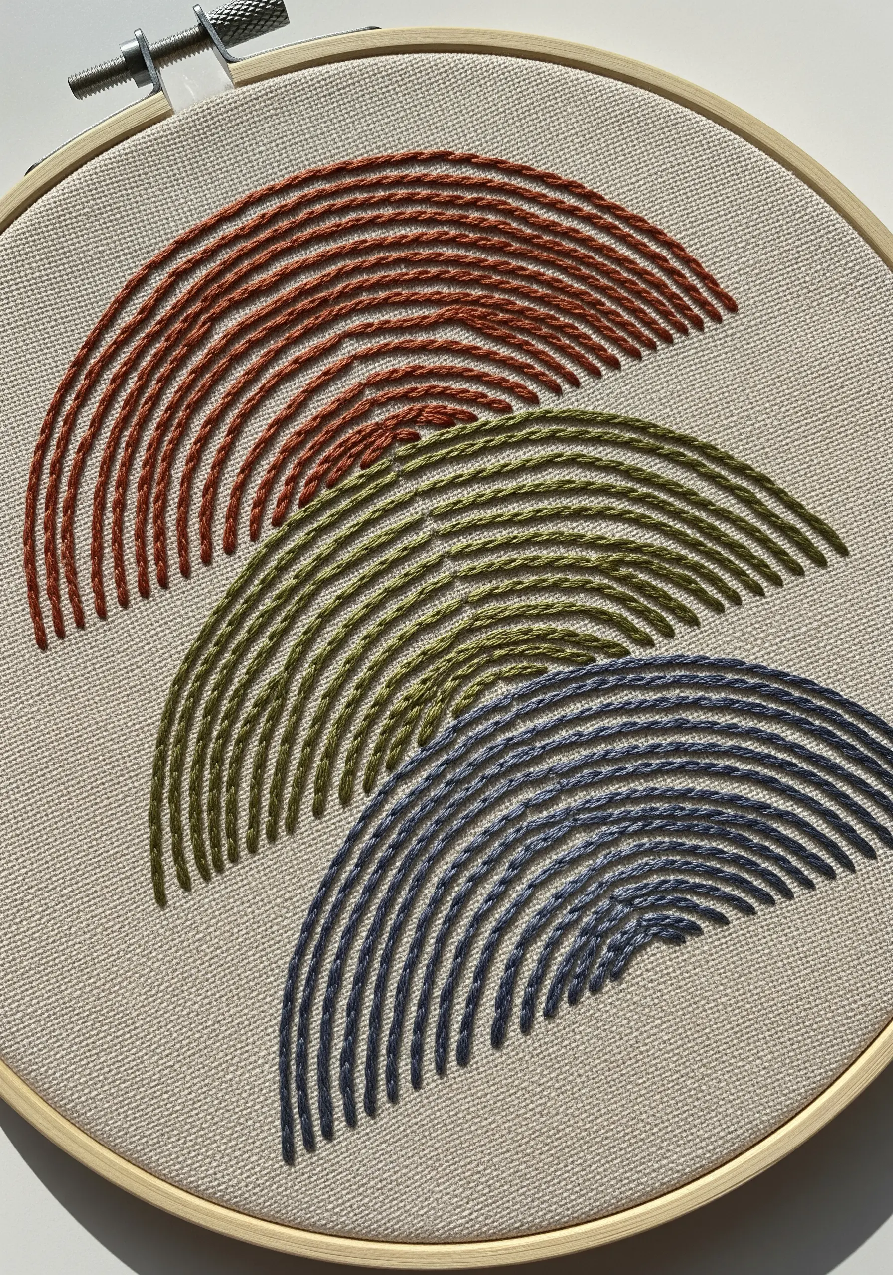 Three sets of stacked, curved arches embroidered in earthy tones of rust, olive, and navy.