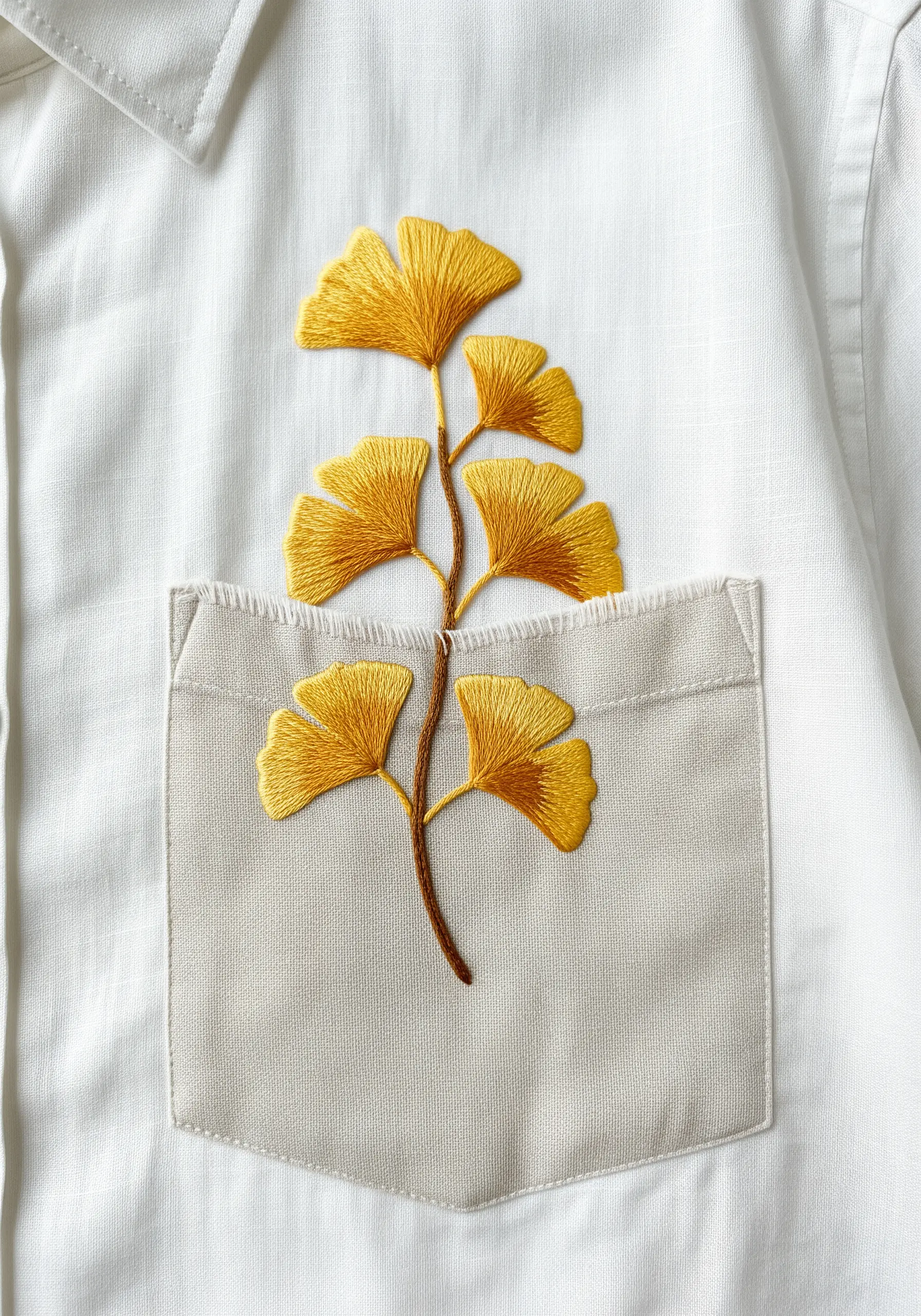 A golden-yellow embroidered ginkgo branch emerging from the pocket of a white button-down shirt.