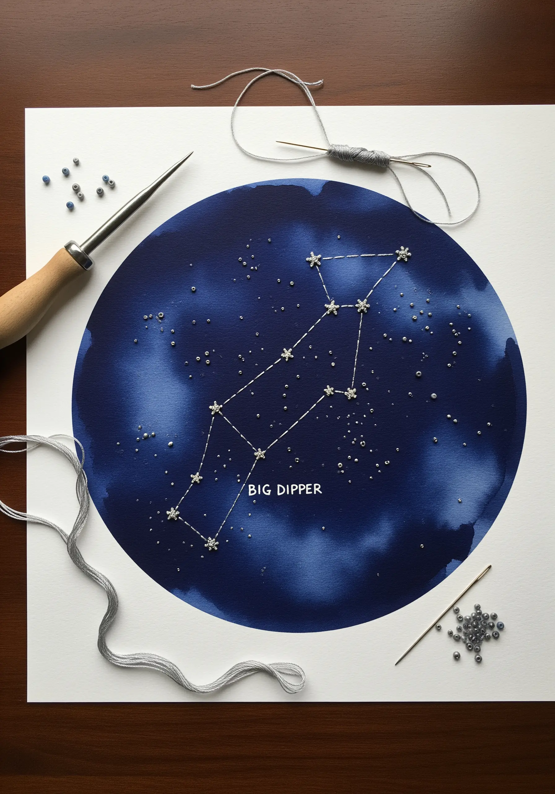 Embroidery on dark blue watercolor paper showing the Big Dipper constellation with silver thread.
