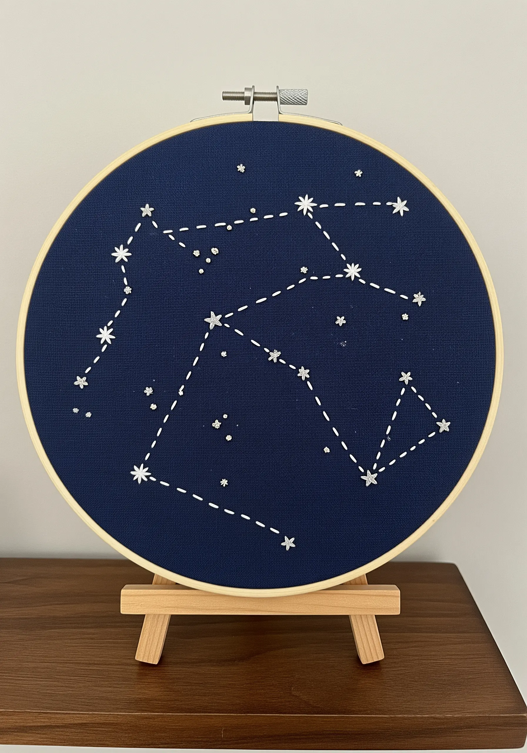 Embroidery hoop with a star constellation stitched in white thread on navy blue fabric.