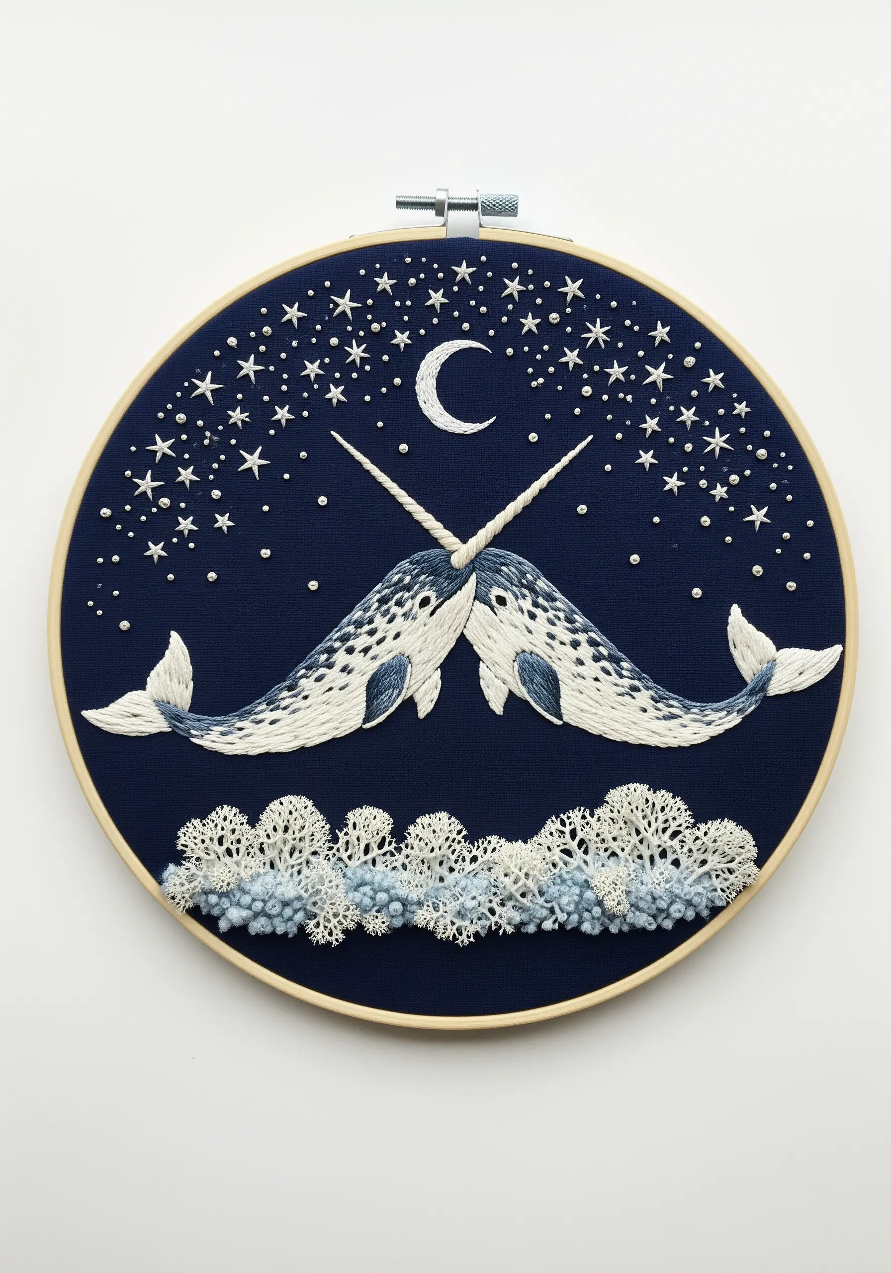 Two narwhals under a starry sky with a crescent moon, stitched on navy blue fabric.