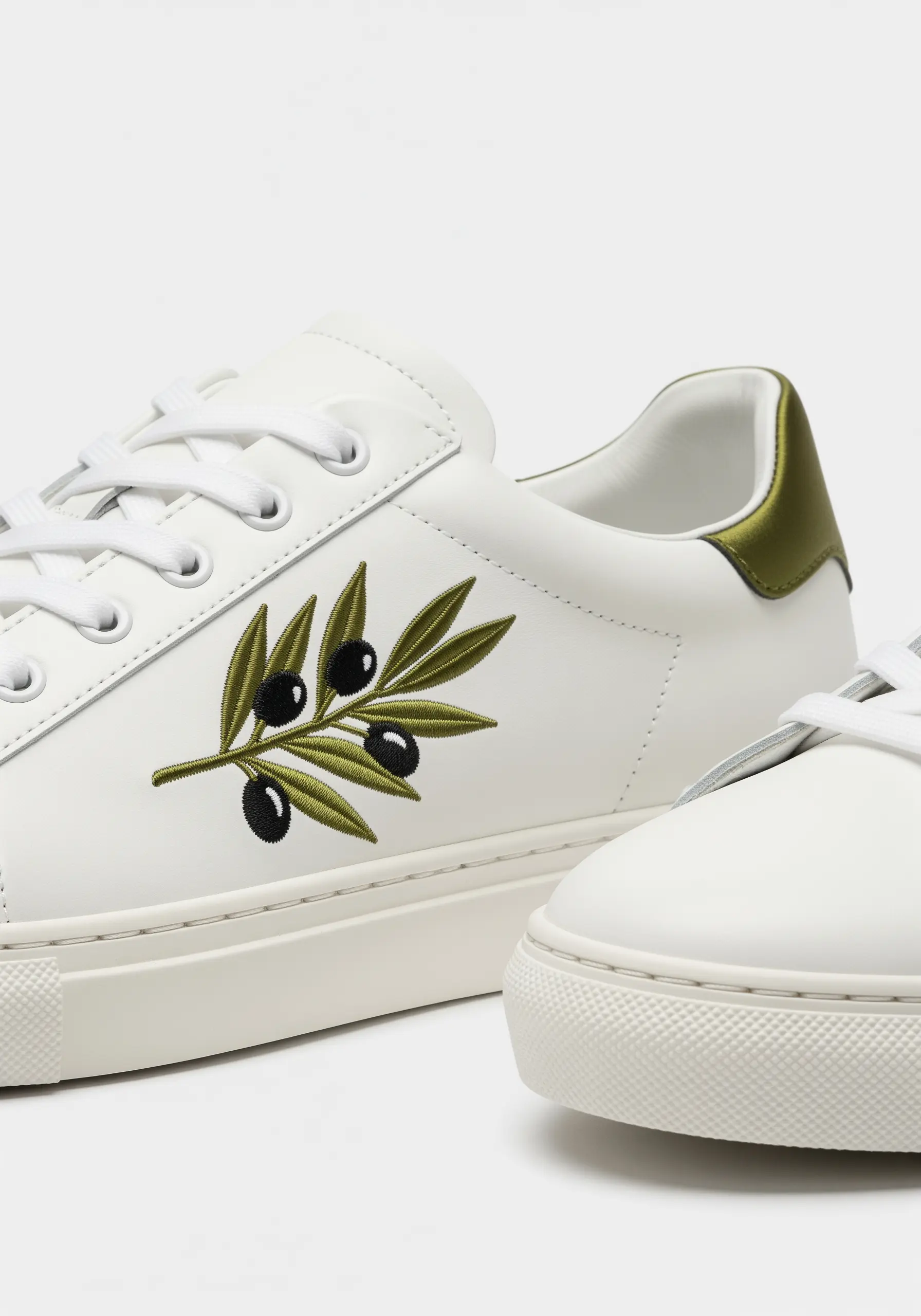 An elegant olive branch with green leaves and black olives embroidered on a white sneaker.