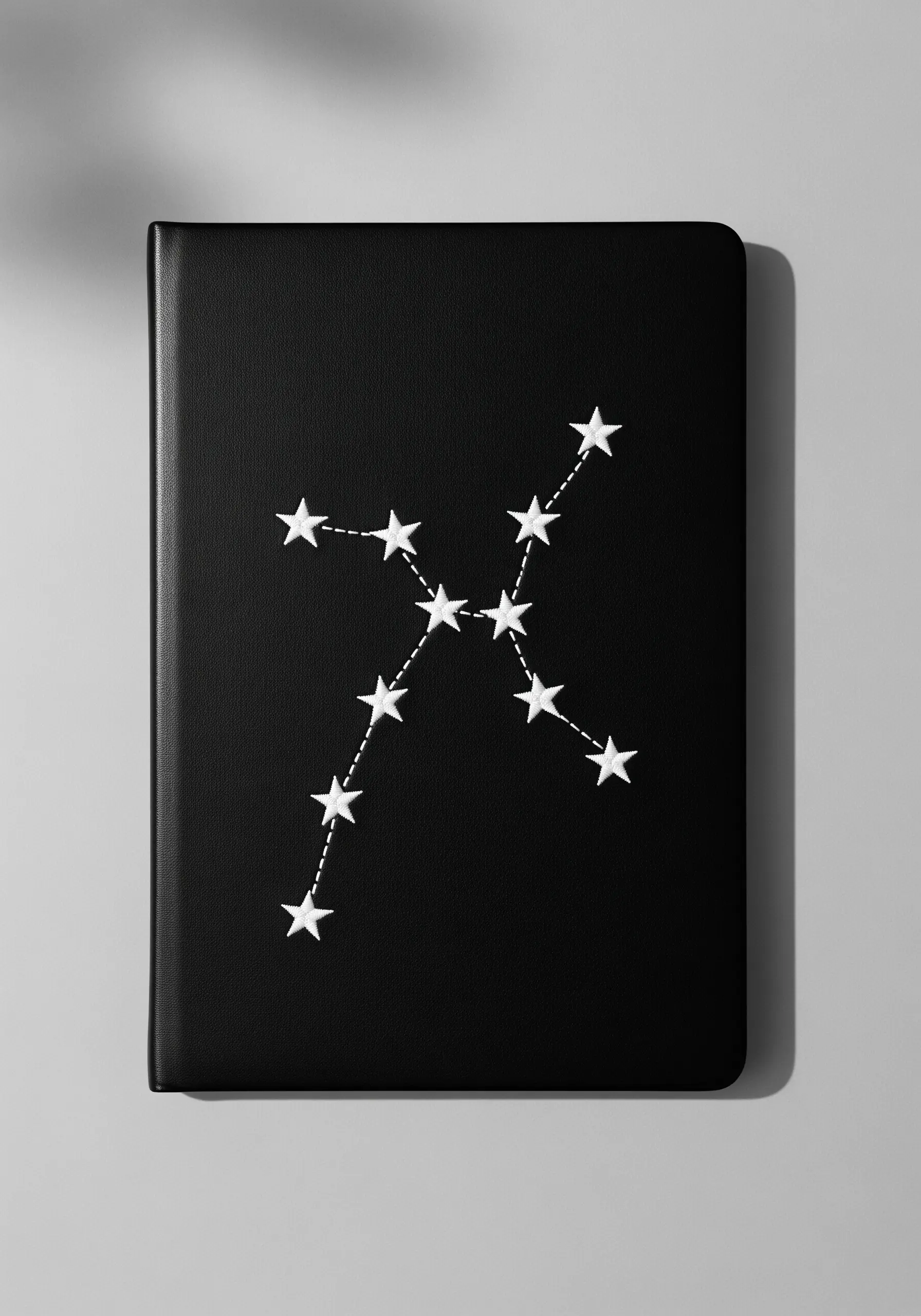 A constellation embroidered in white thread on a black notebook cover.