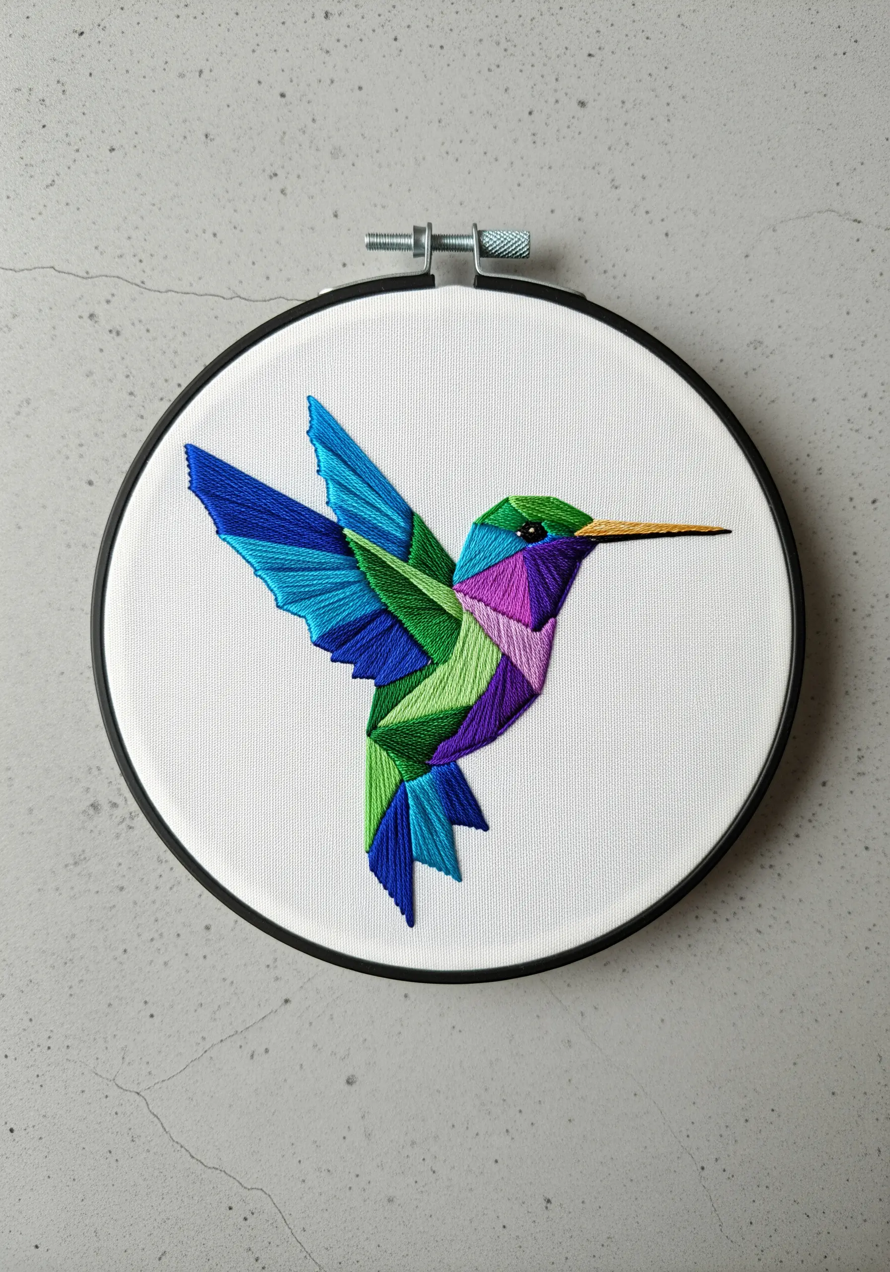 A geometric hummingbird embroidered with vibrant, color-blocked satin stitch sections.