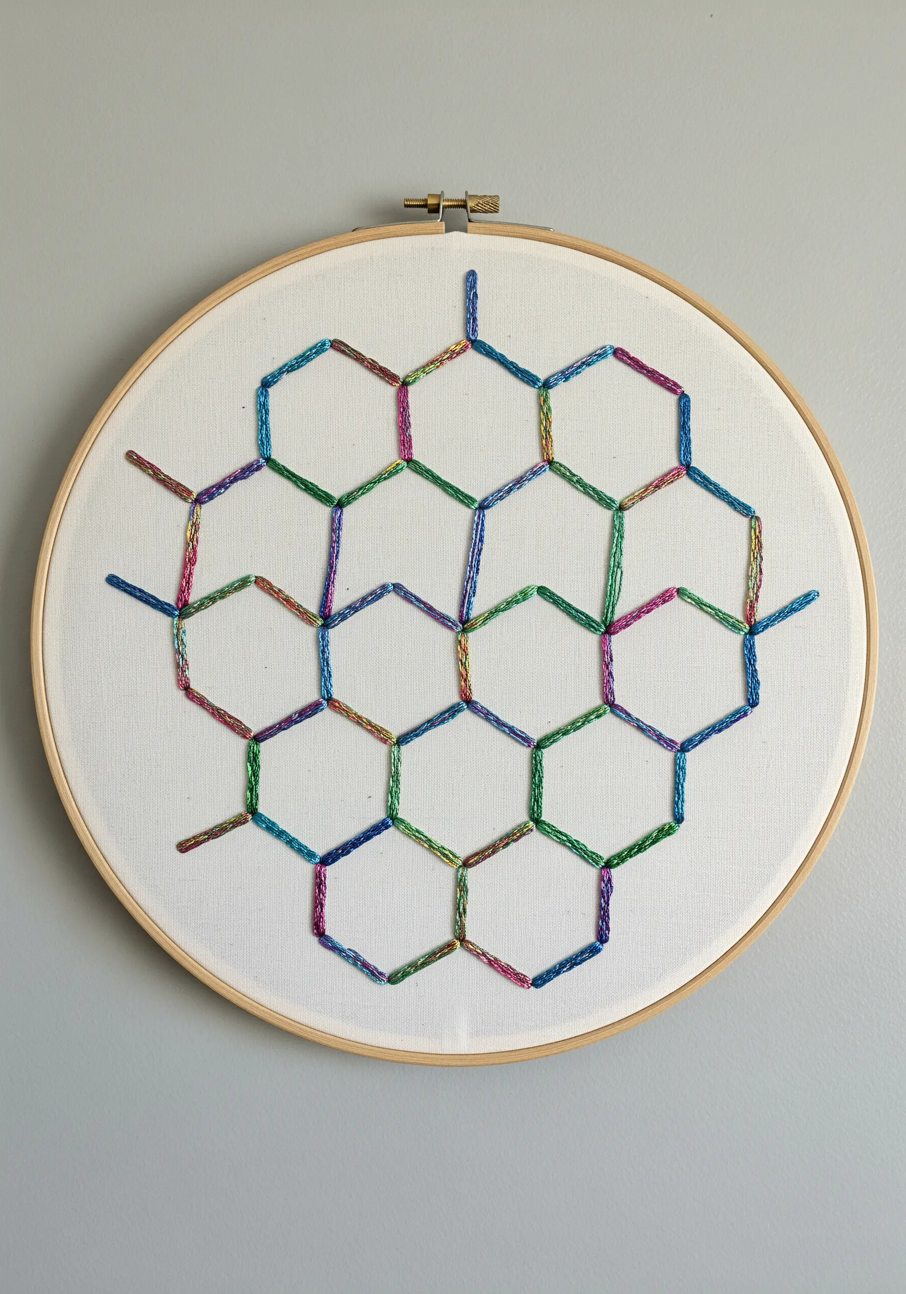 Embroidery hoop with a honeycomb geometric pattern stitched in a multi-colored variegated metallic thread.