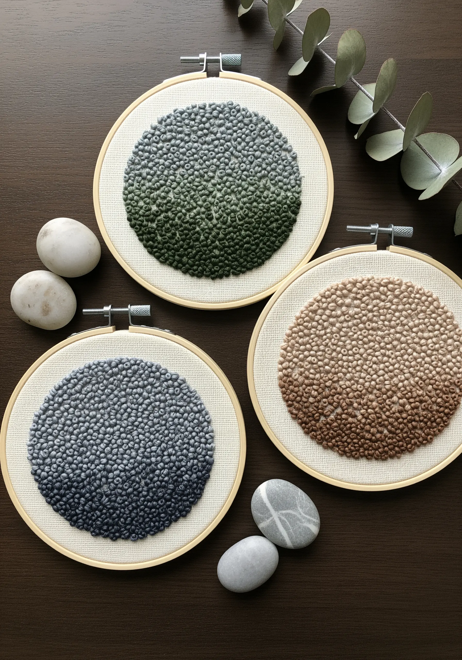Three embroidery hoops filled with French knots in green, blue, and brown color gradients.