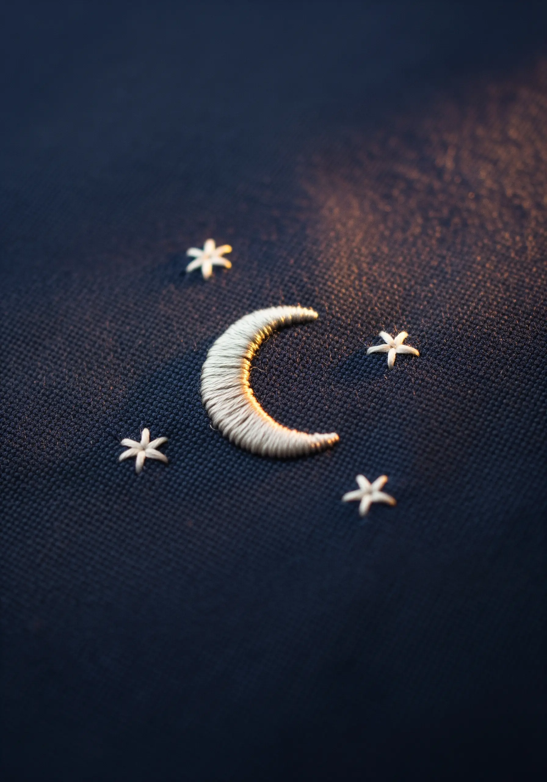 A satin-stitched crescent moon with star stitches on dark blue fabric.