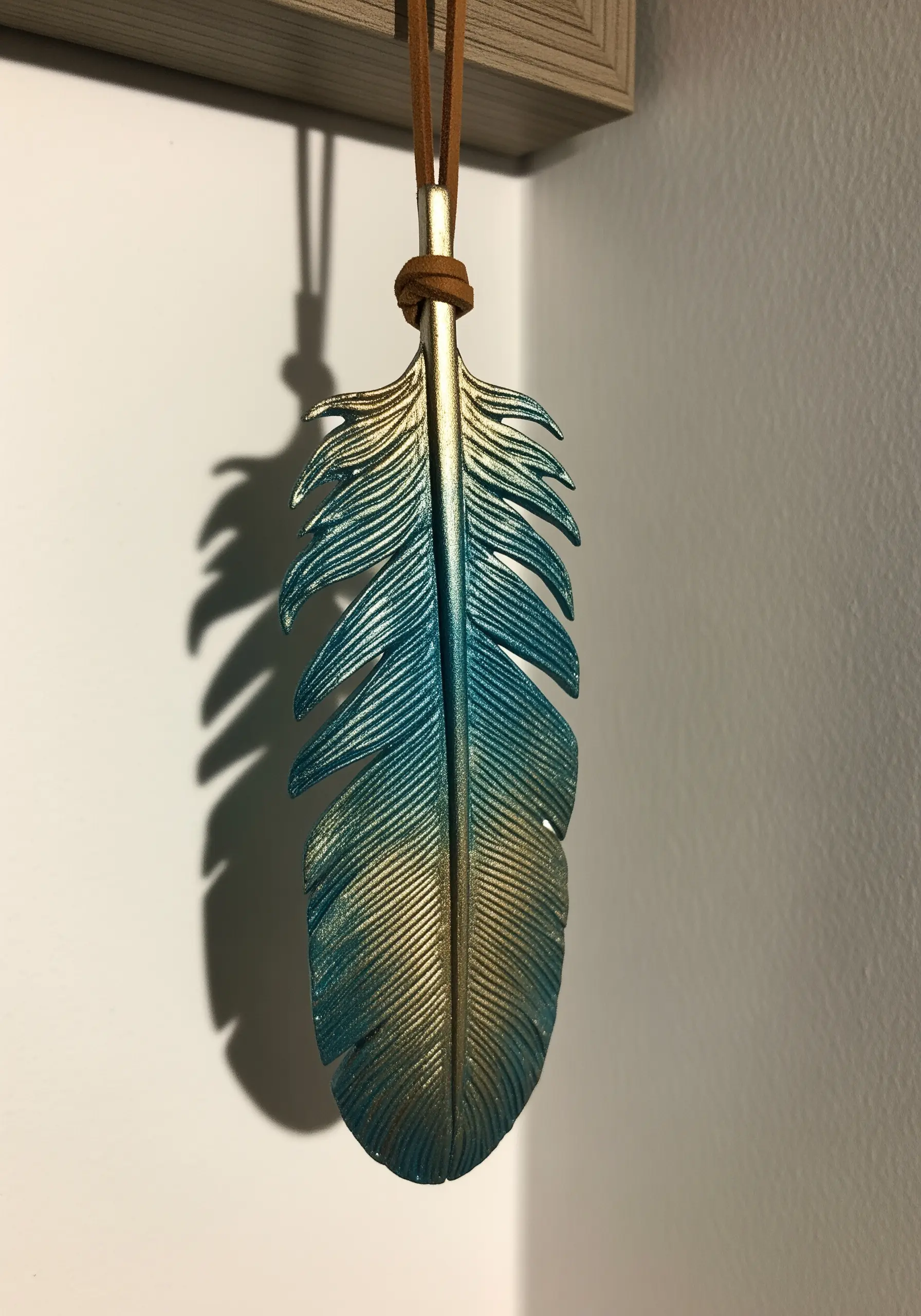 A feather ornament with a metallic gradient finish, shifting from gold to teal blue.