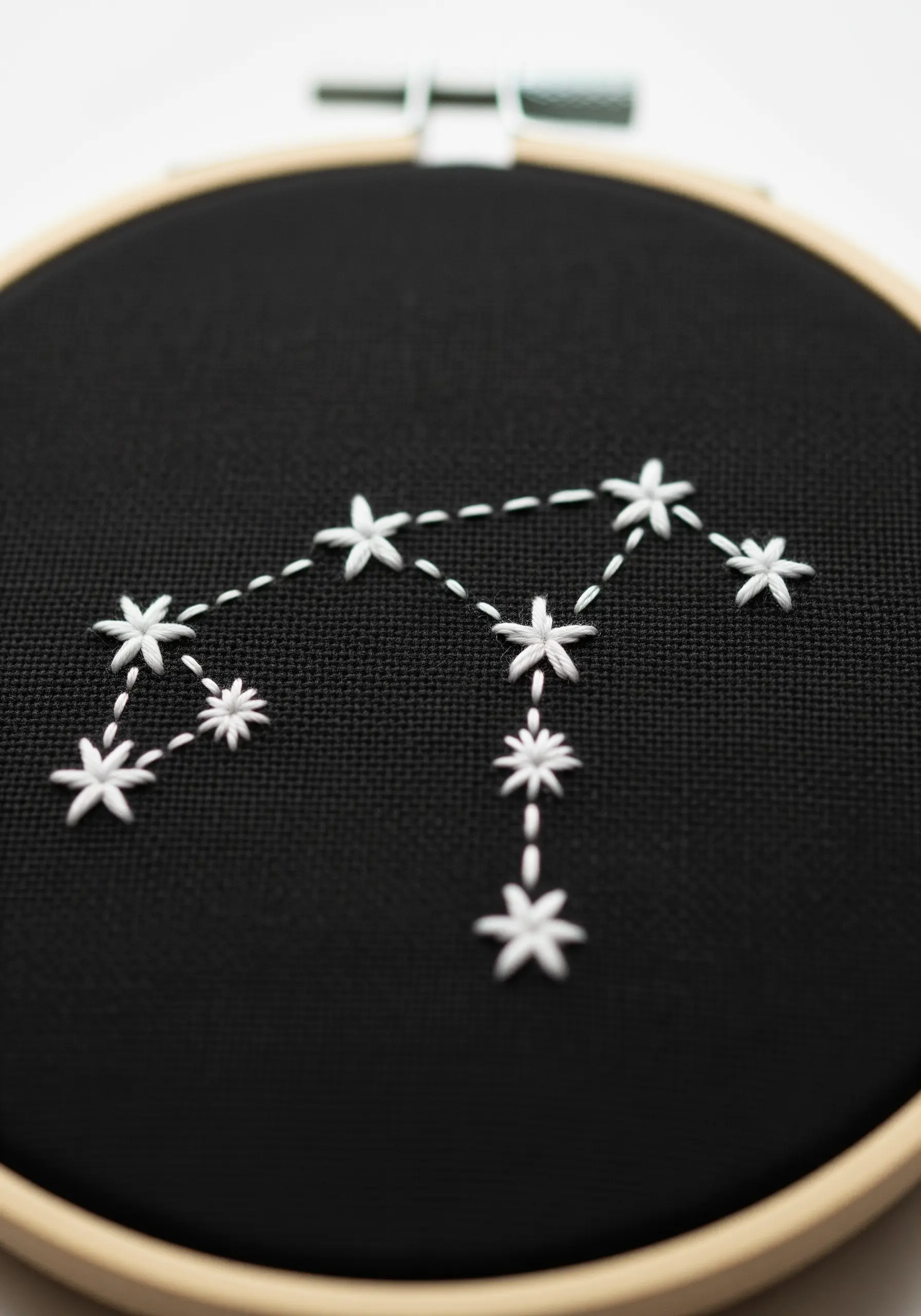 A white thread constellation with lazy daisy stars on black fabric.