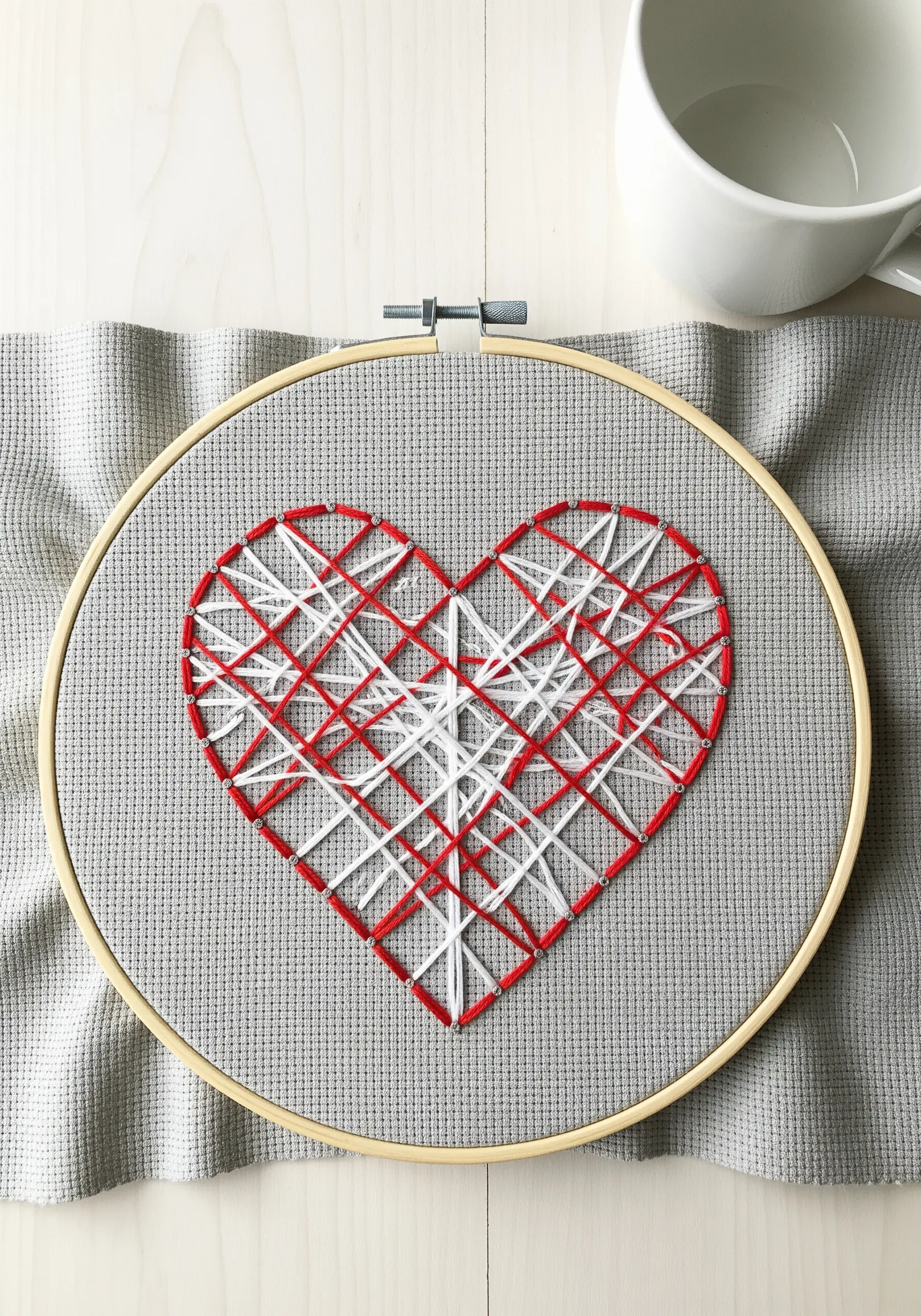 A heart filled with an intersecting grid of red and white straight stitches on gray fabric.