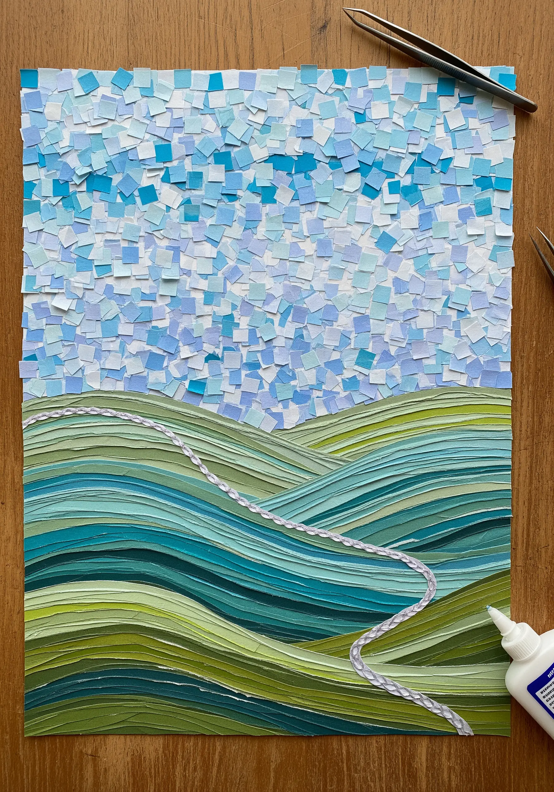 A landscape collage with a mosaic paper sky and layered paper hills.