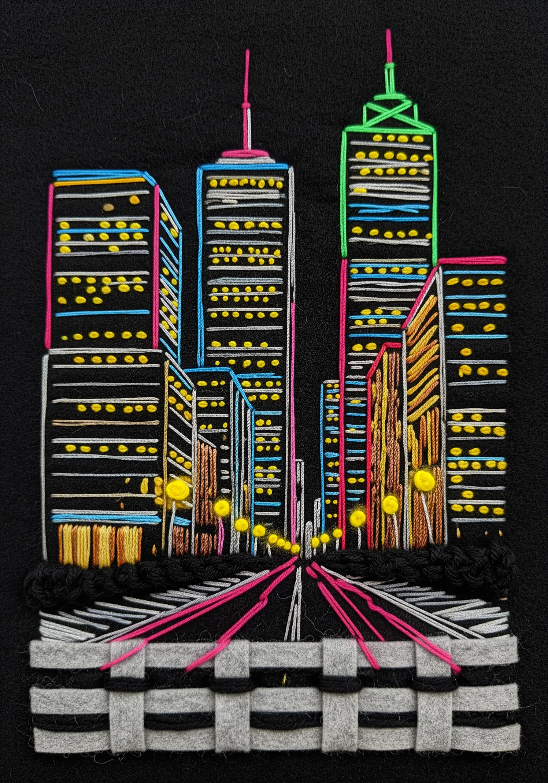 Embroidered neon cityscape on black fabric with a woven felt fence.