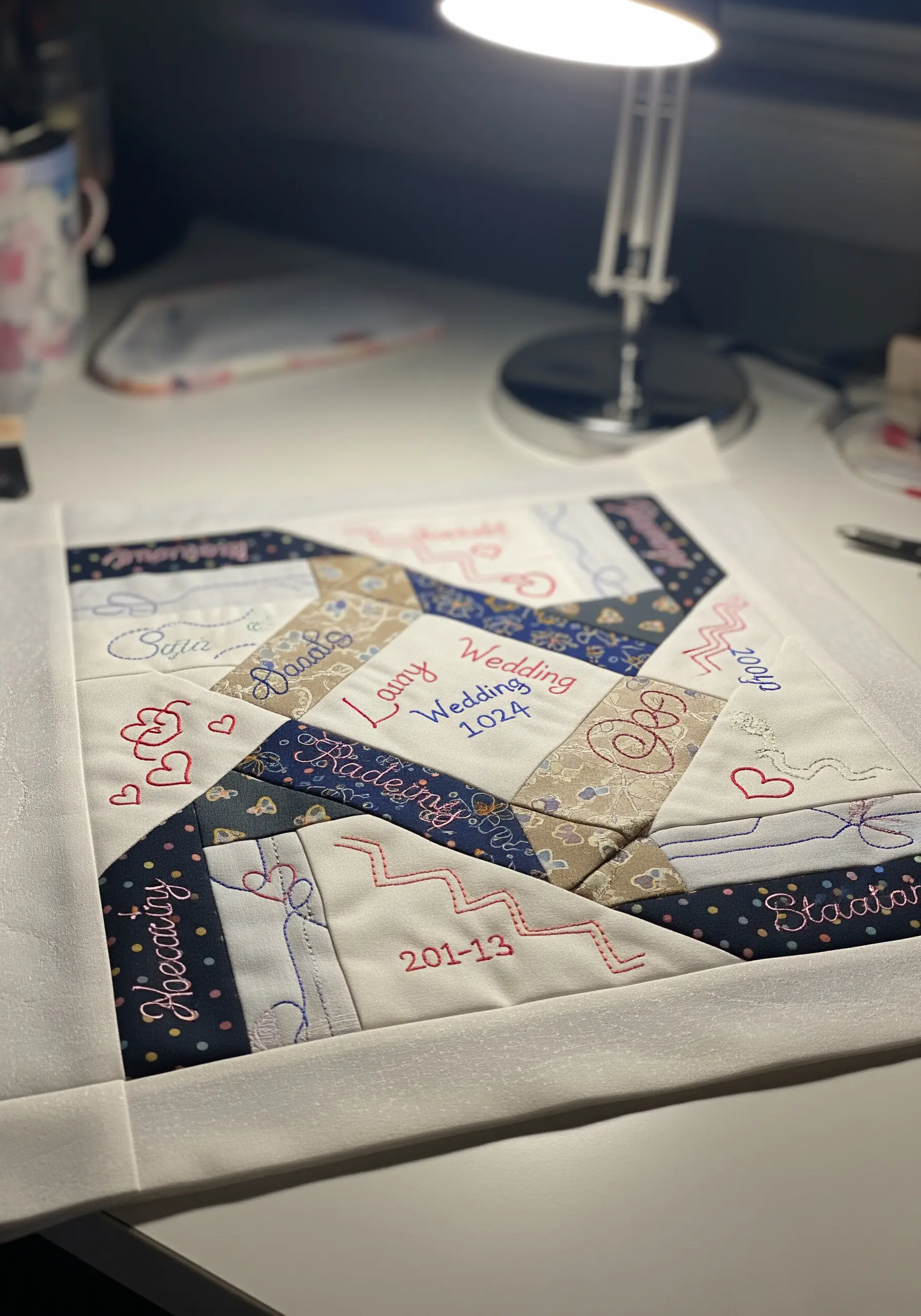 A quilt block in progress, featuring pieced fabrics with handwritten names and dates embroidered on top
