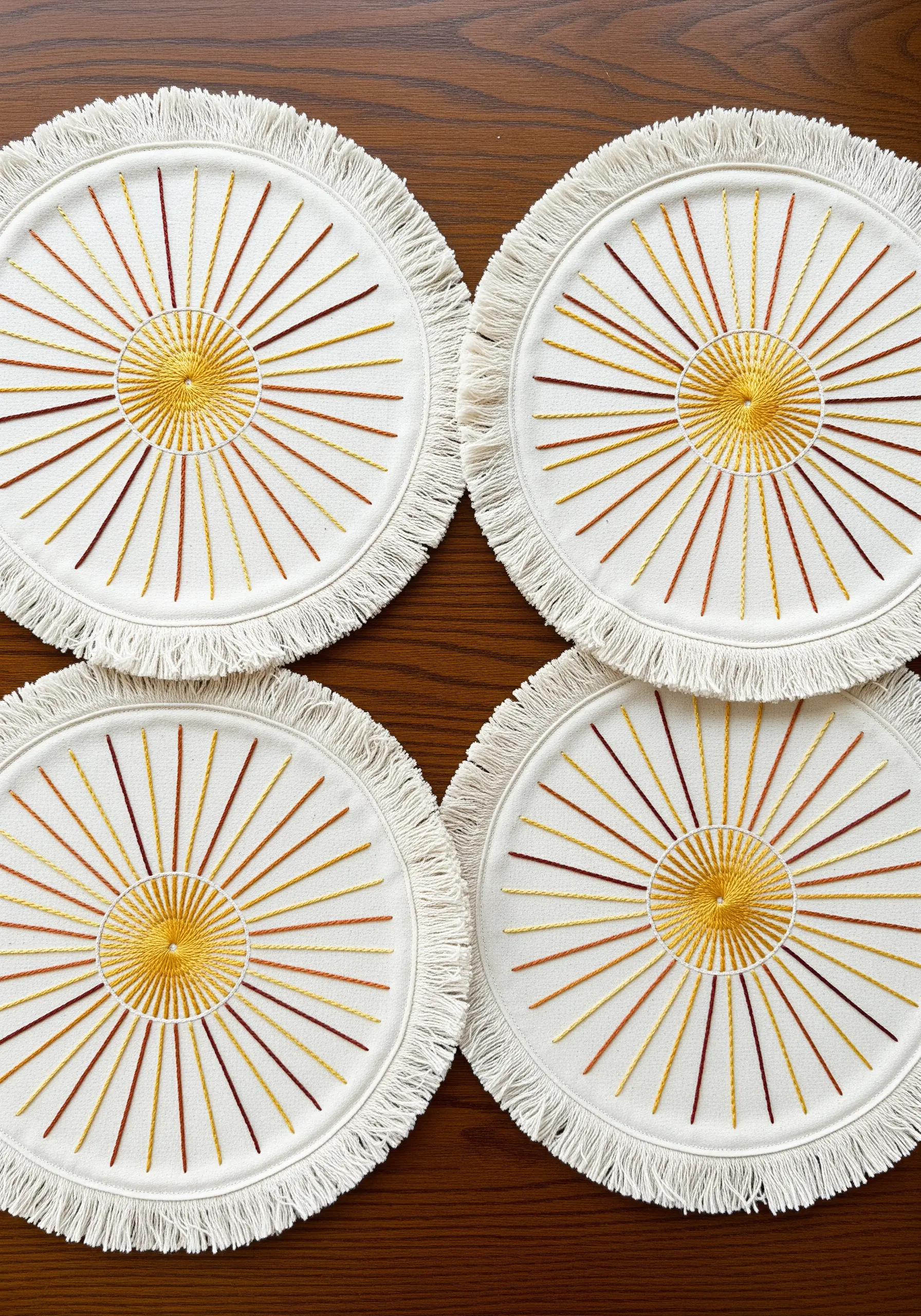 Four round coasters with embroidered sunbursts in yellow, orange, and red thread.