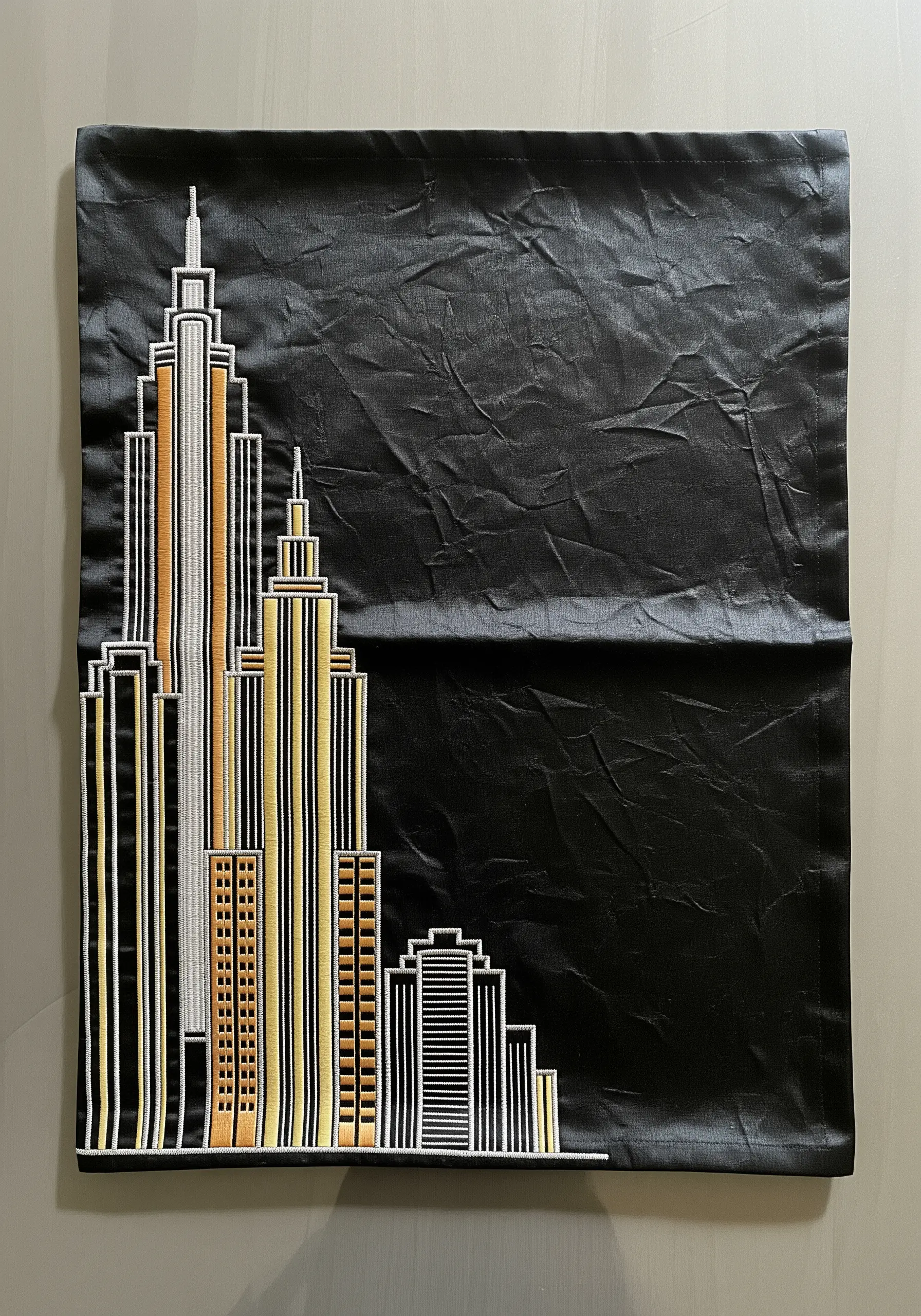 A black placemat featuring an embroidered Art Deco city skyline in metallic threads.