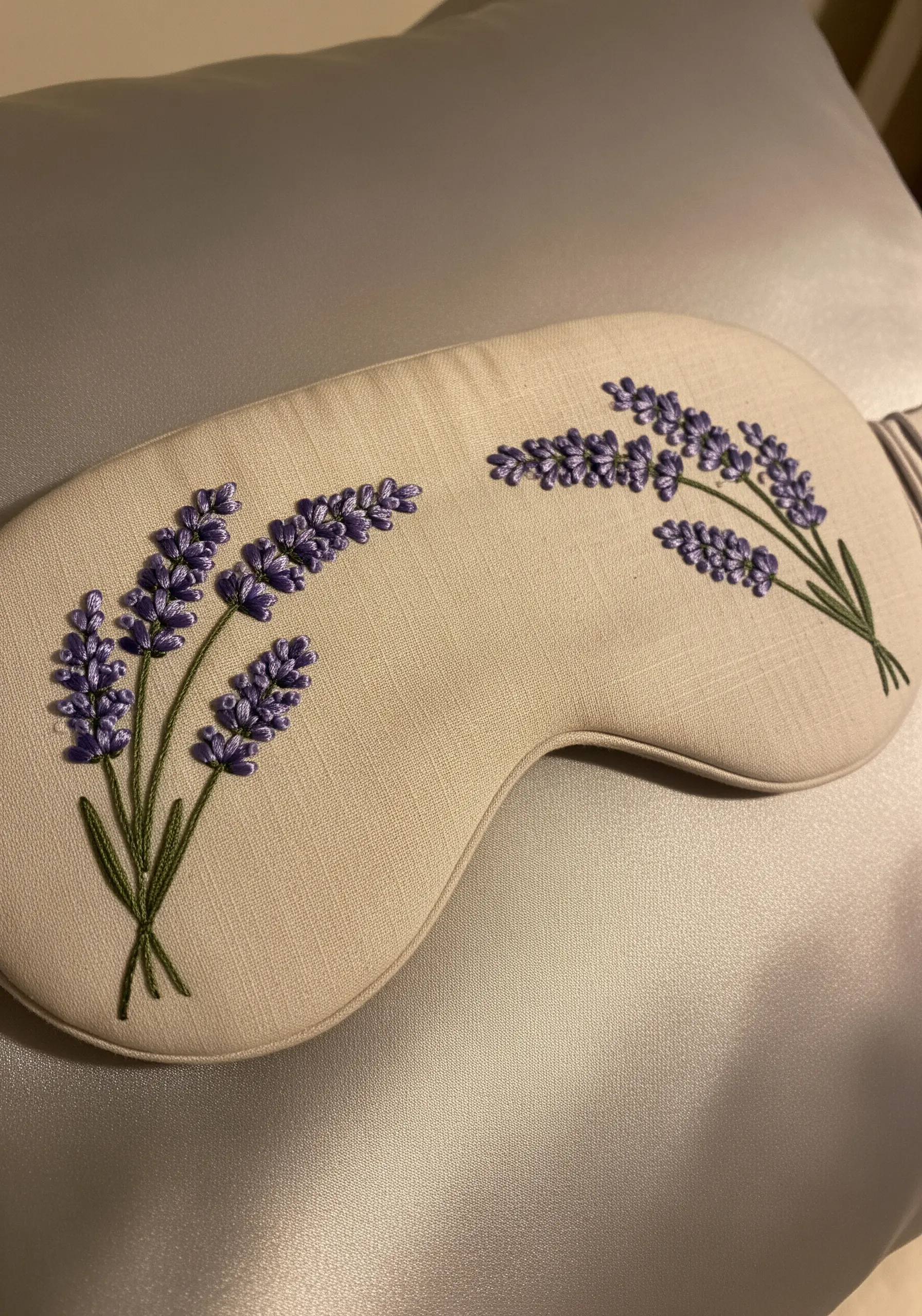 A handmade sleep mask decorated with two small bouquets of embroidered lavender.