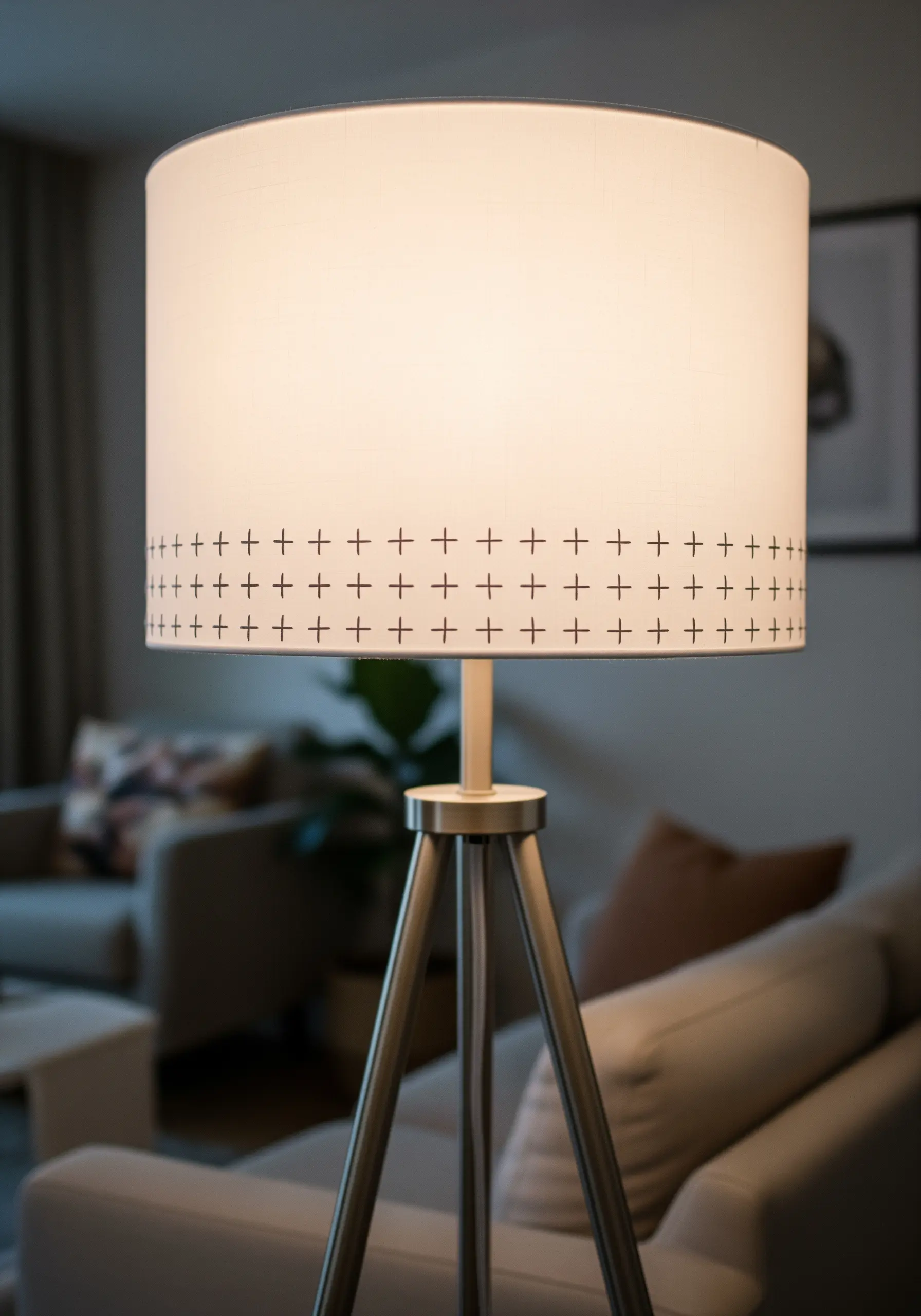 A white drum lampshade with a simple black cross-stitch pattern around the bottom edge.