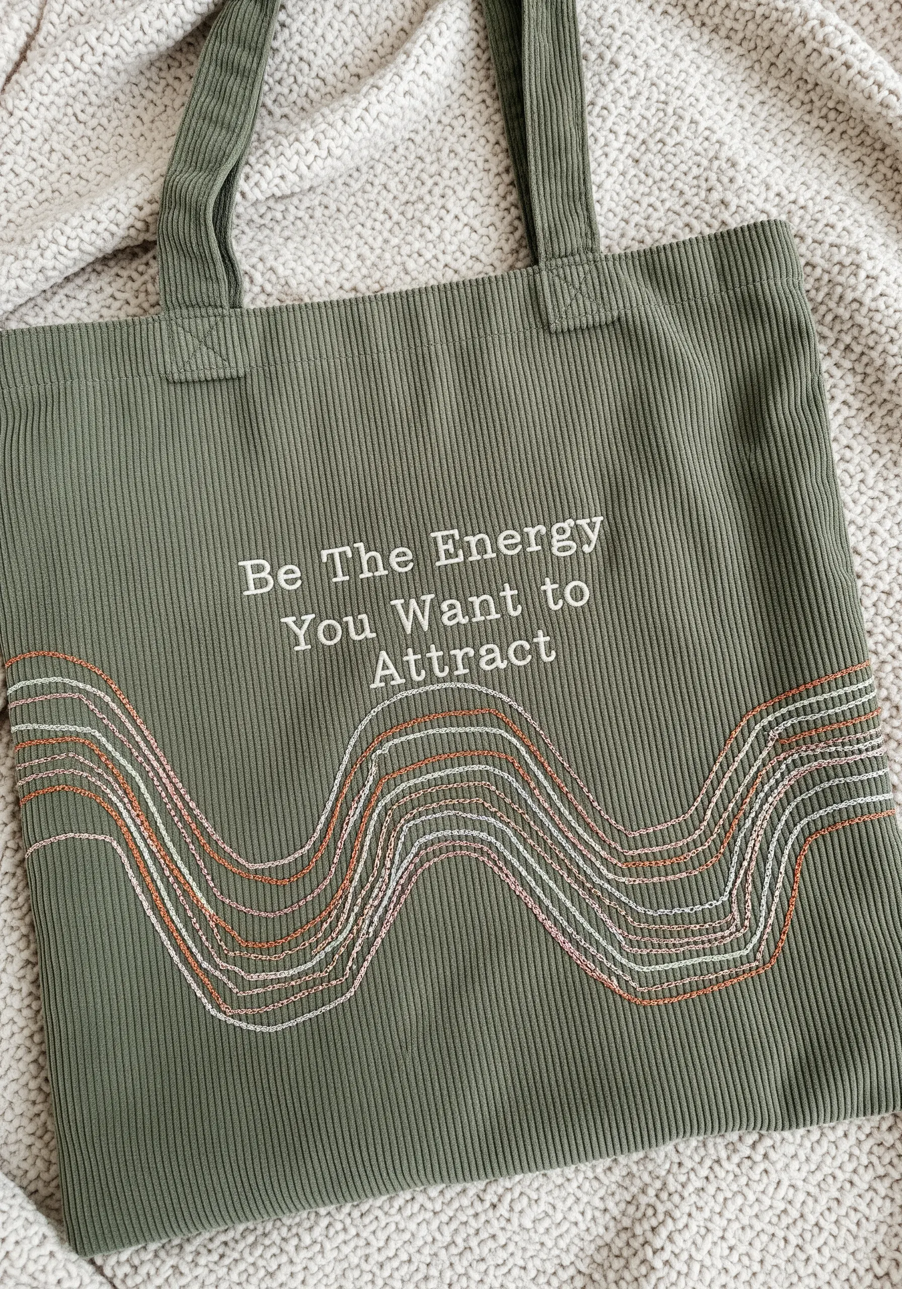 Quote embroidered on a green corduroy tote with abstract waves in metallic and pastel threads.