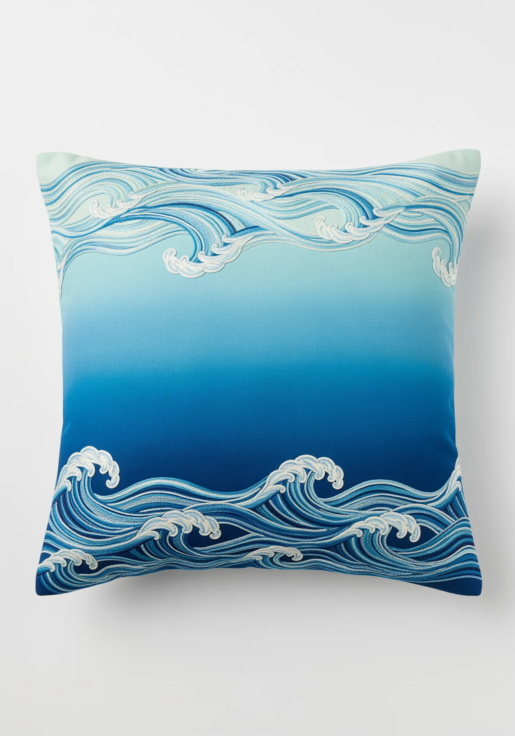 Stylized ocean waves embroidered in shades of blue and white on an ombré blue cushion