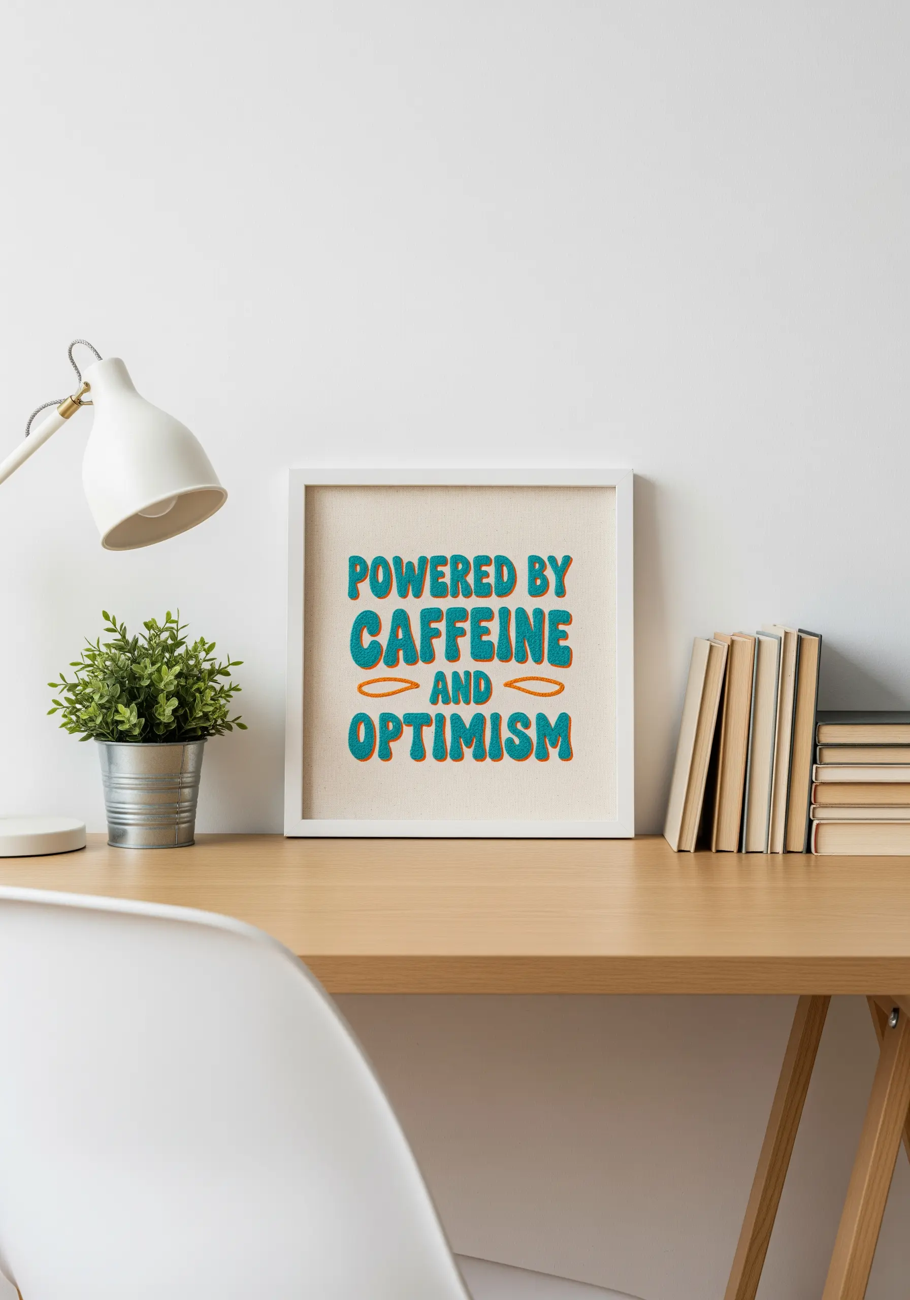 Framed embroidery of a retro-style quote in teal and orange on a modern desk.