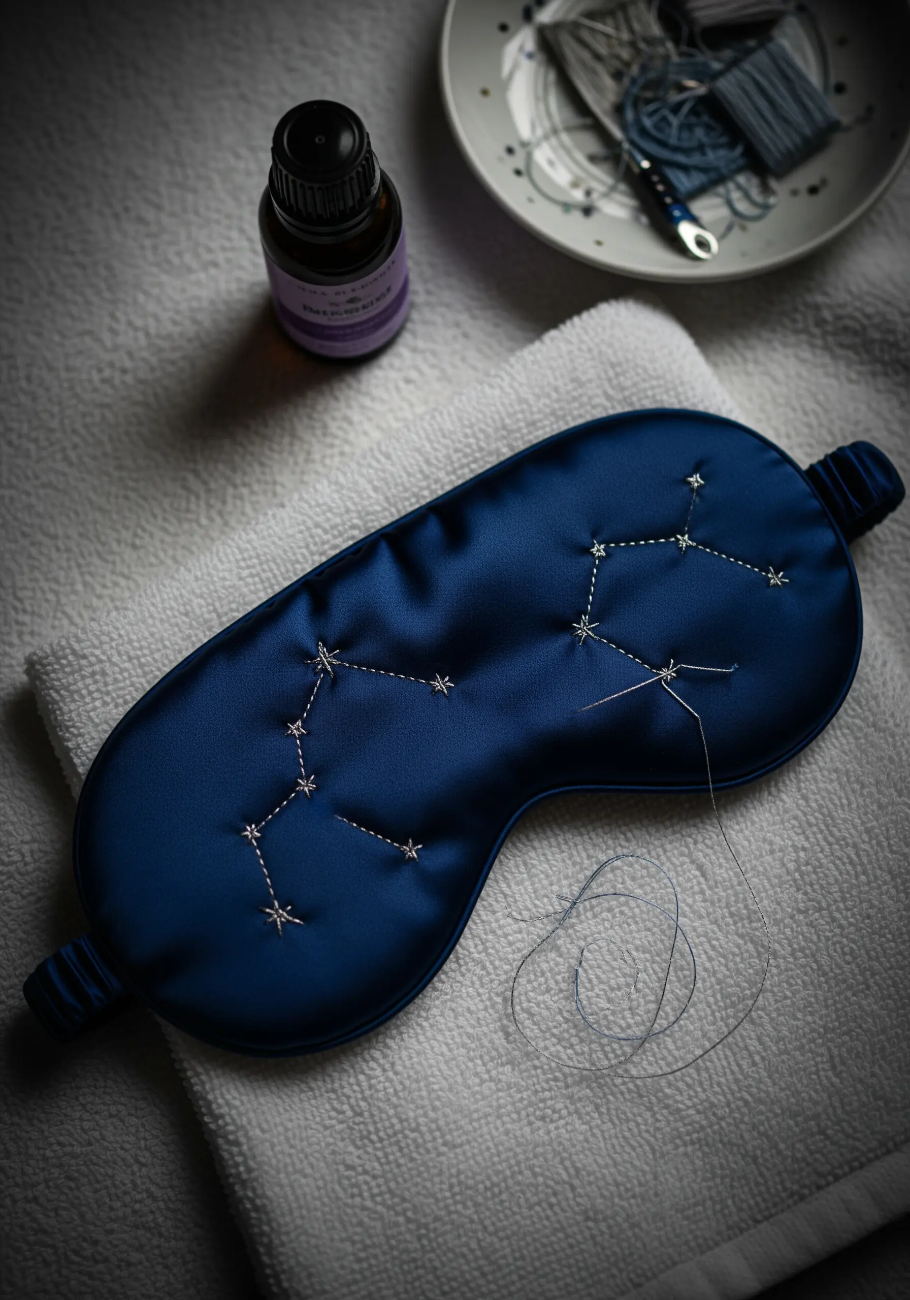 Embroidering a star constellation with silver thread onto a navy blue silk sleep mask