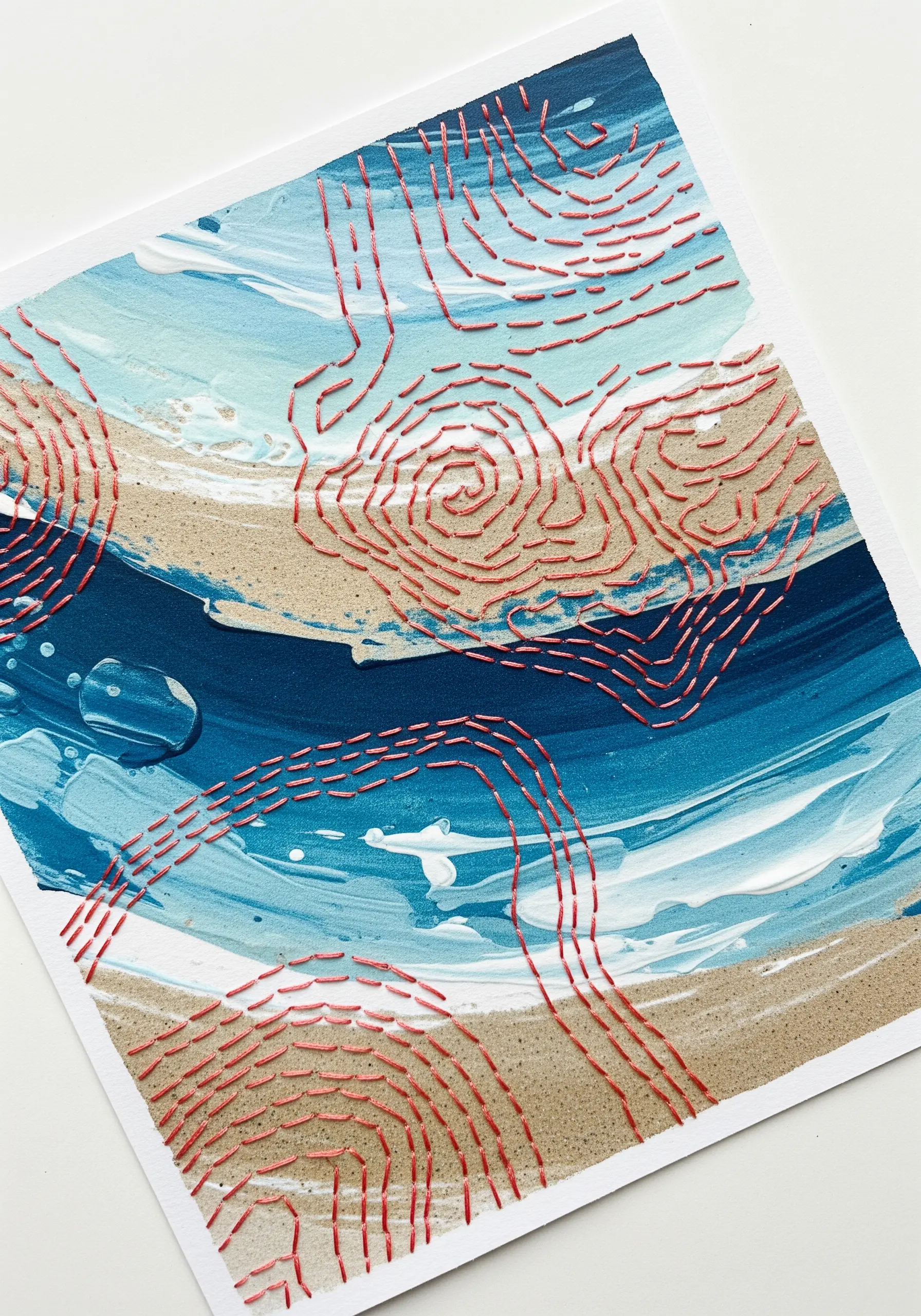 Red running stitches creating topographic lines over an abstract blue and sand painted background.
