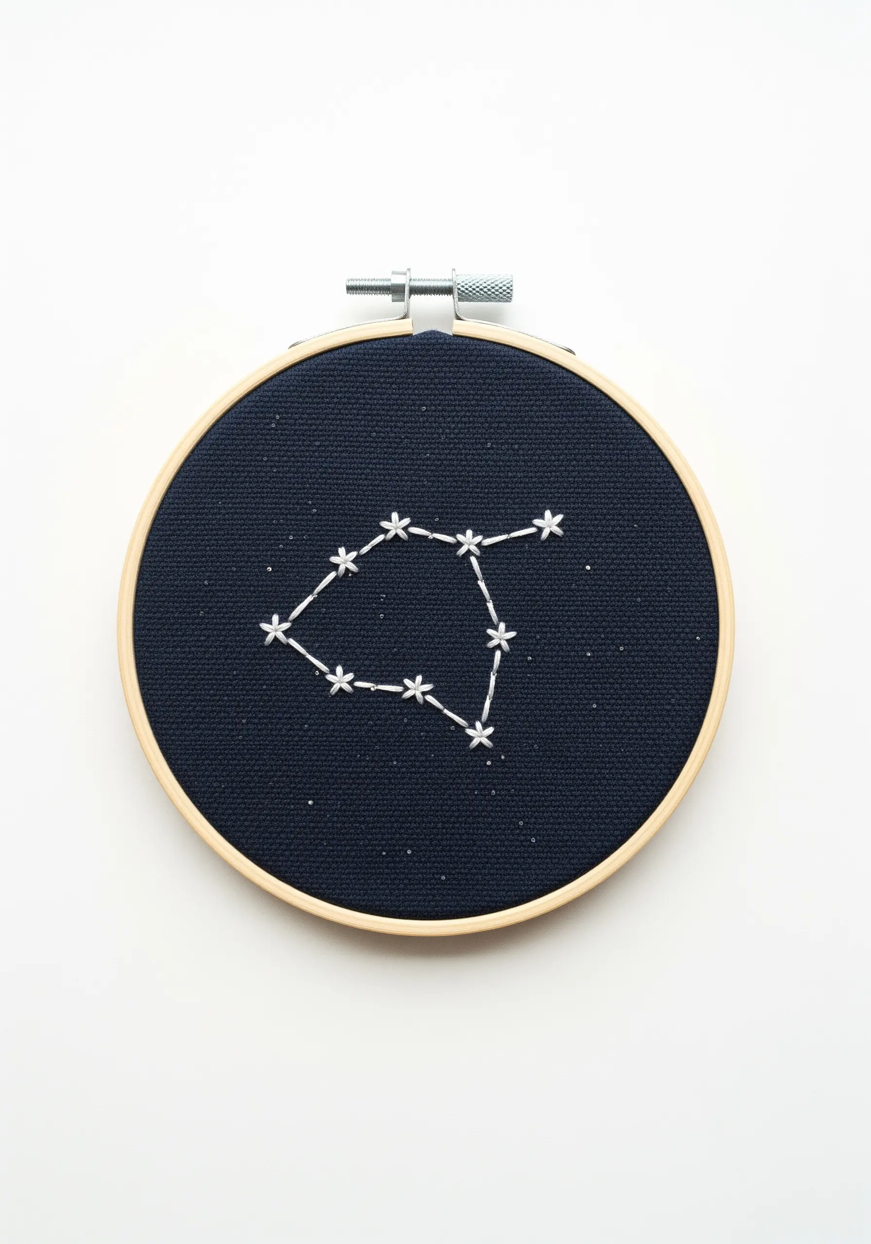 A star constellation embroidered in white thread on a dark navy blue fabric hoop.