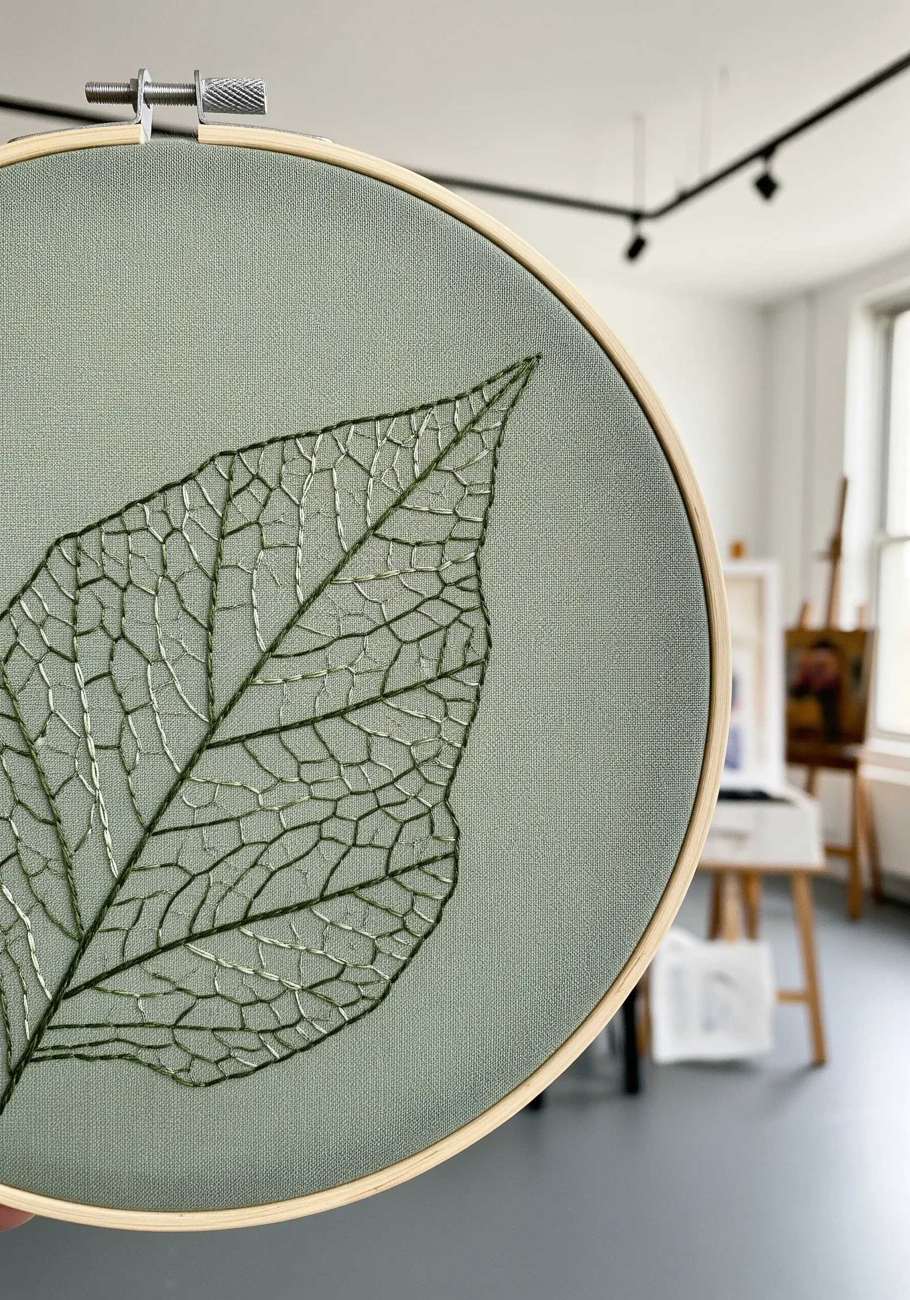 Detailed embroidery of a leaf skeleton with fine veins on sage green fabric.