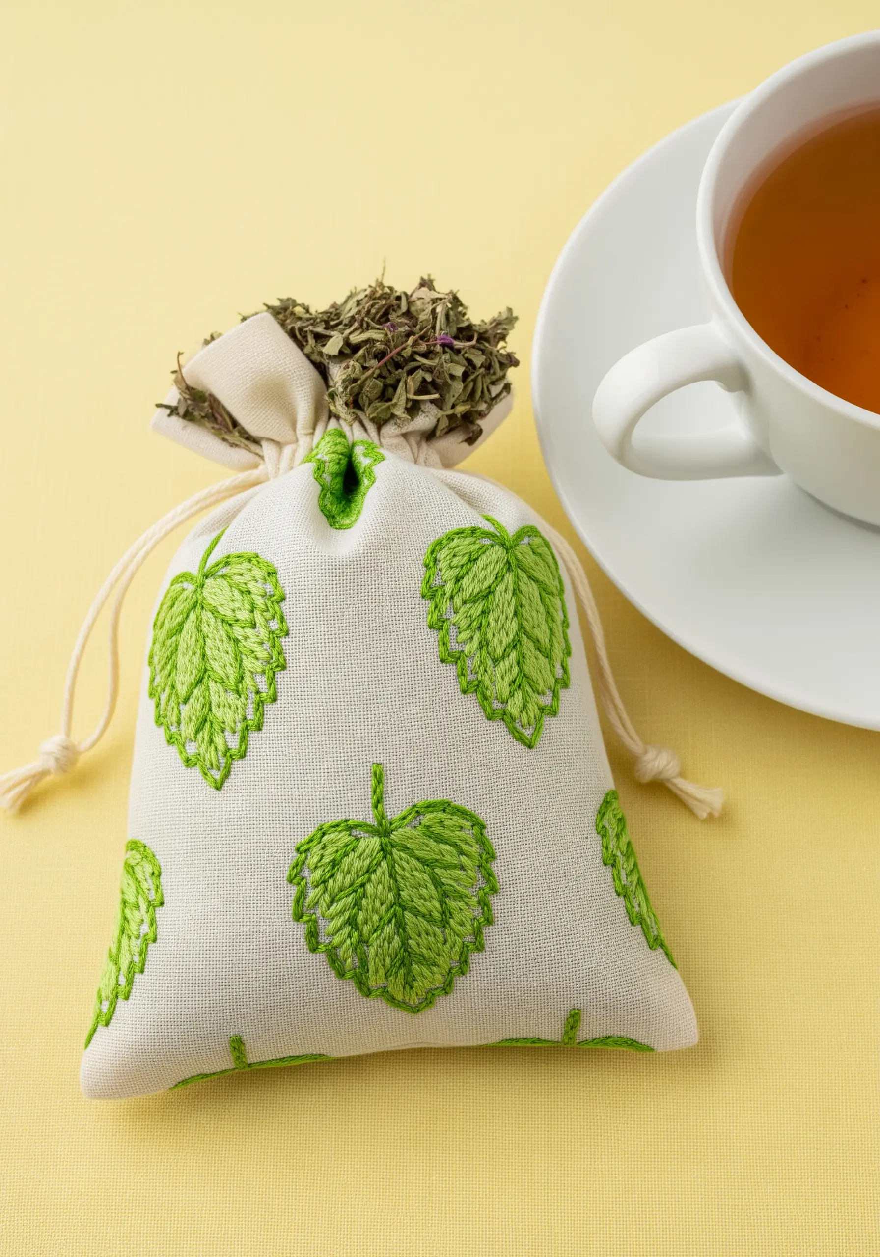 A small fabric pouch for tea embroidered with a pattern of green hops leaves.