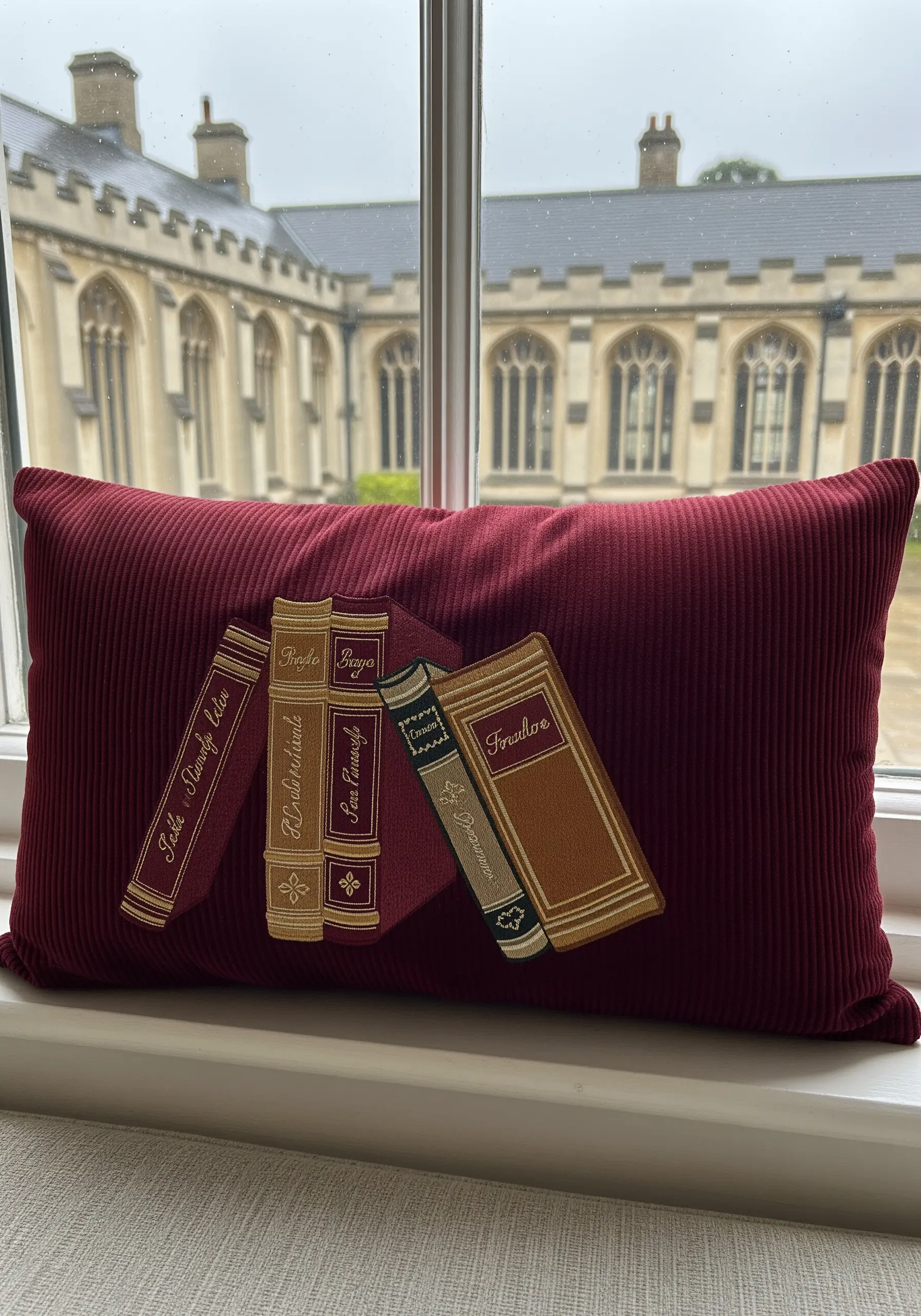 Four embroidered antique book spines leaning against each other on a dark red corduroy cushion.