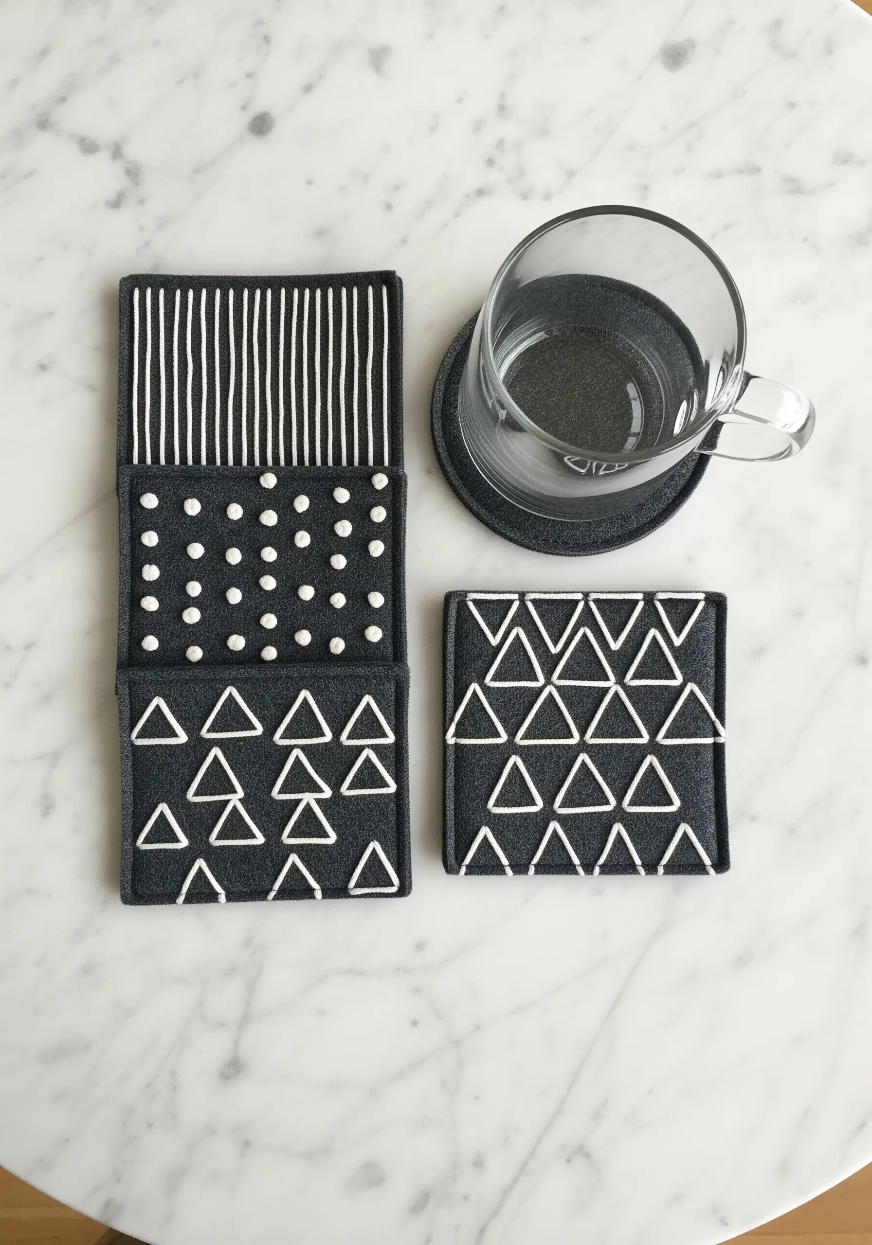 A set of dark gray felt coasters with minimalist geometric patterns stitched in white thread.