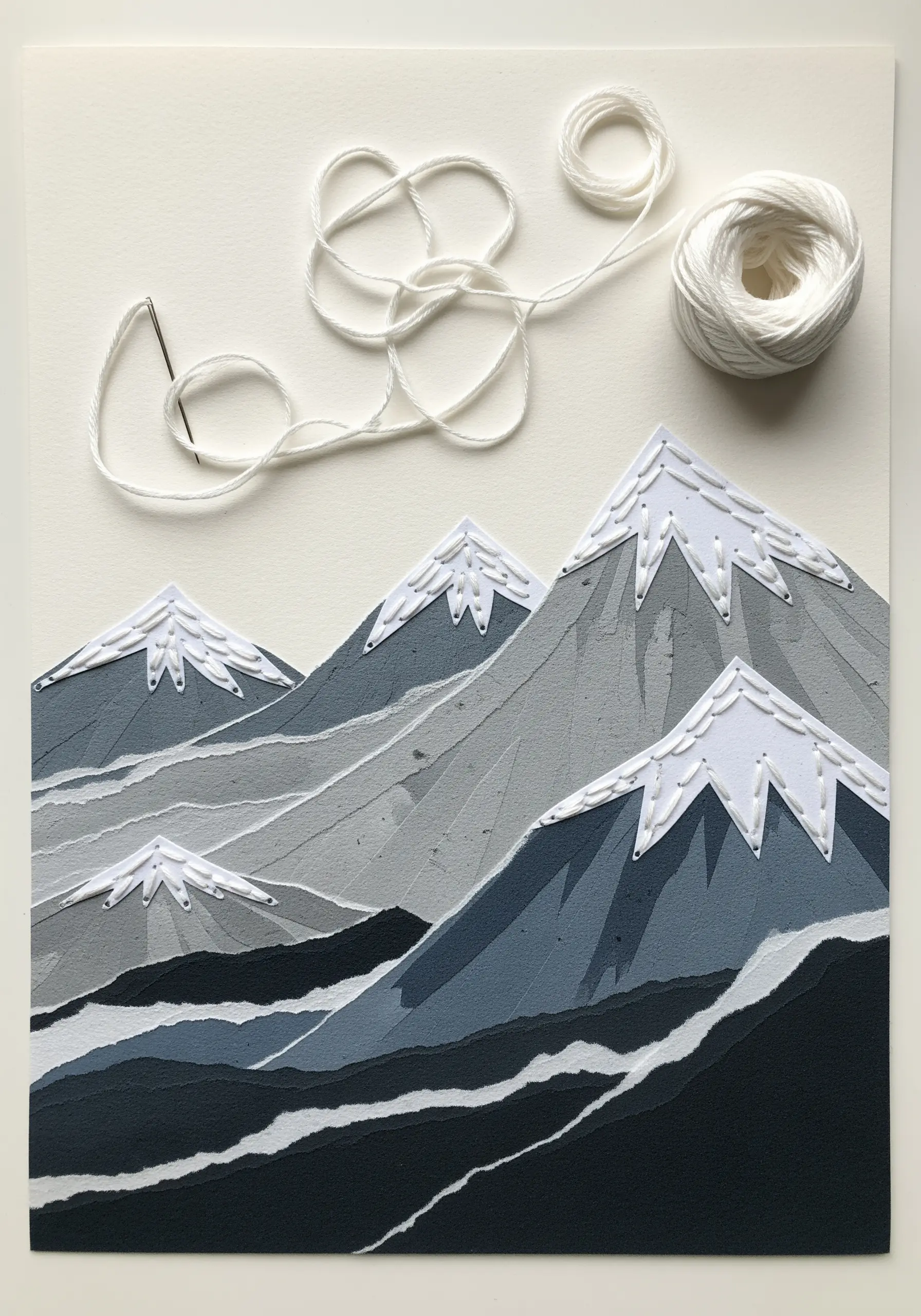 Layered paper mountains in shades of grey with white stitched snow.